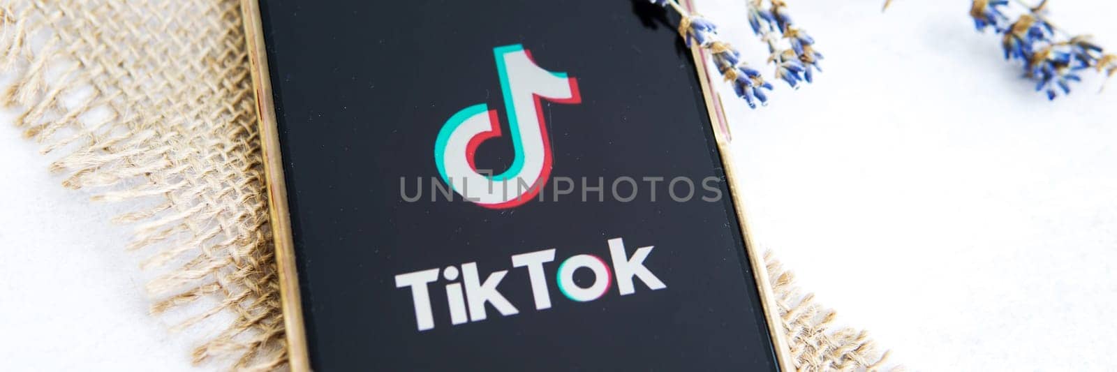 Tver, Russia-August 5, 2020, the tik tok logo on the smartphone screen on a light background with lavender flowers. Tick-Tok icon. logo of the current app. Tiktok social network. by Annu1tochka