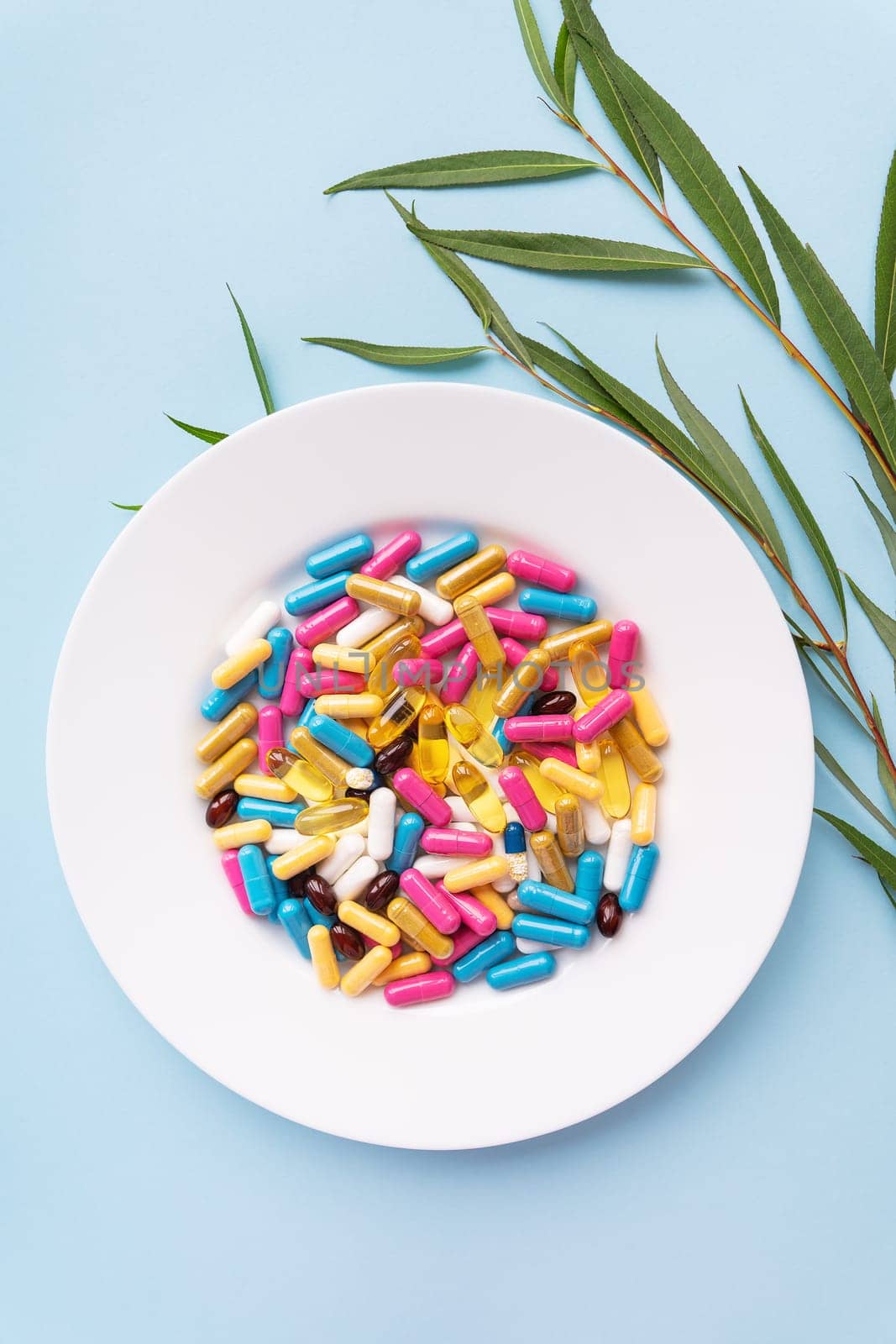 Many colorful pills, nutritional supplements in a white plate on a blue background. Prescription medicine, vertical photo