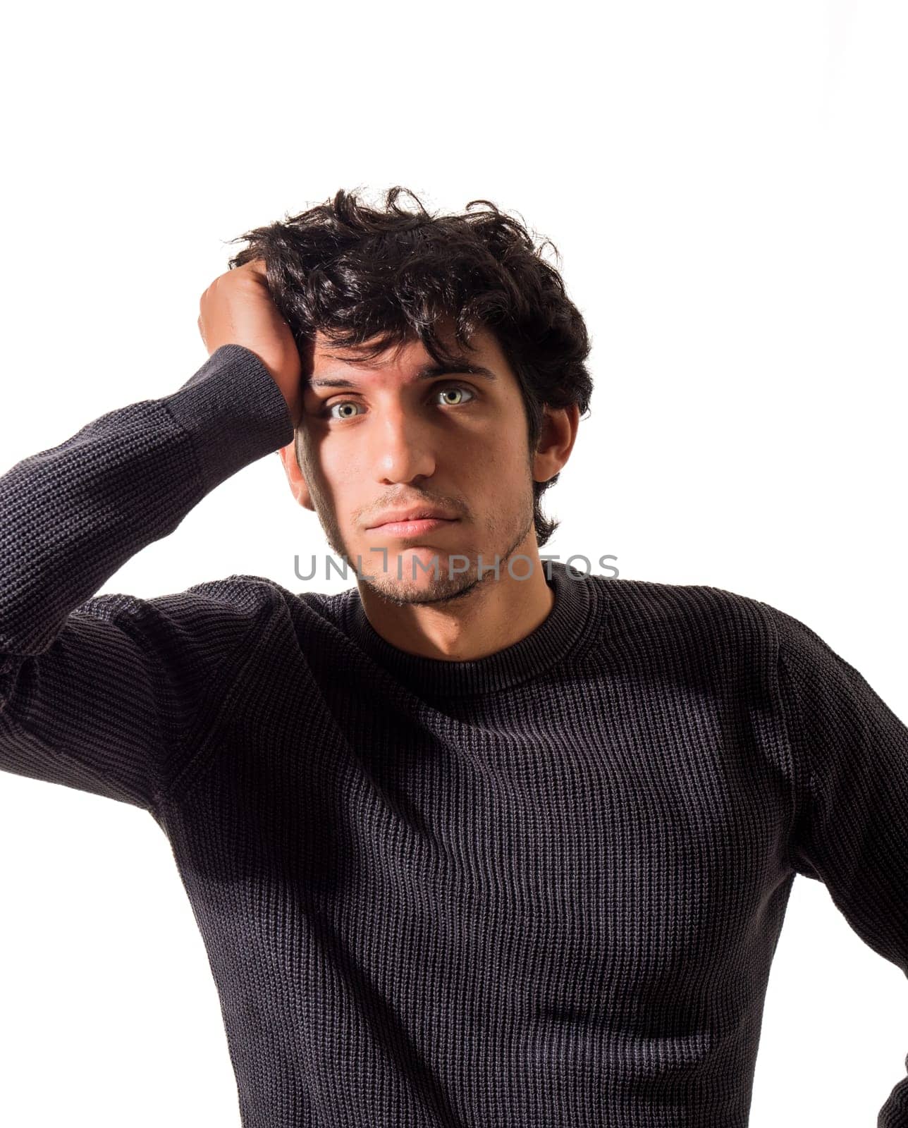 A young attractive man with curly hair is posing for a picture, with a puzzled, indecisive expression, isolated on white