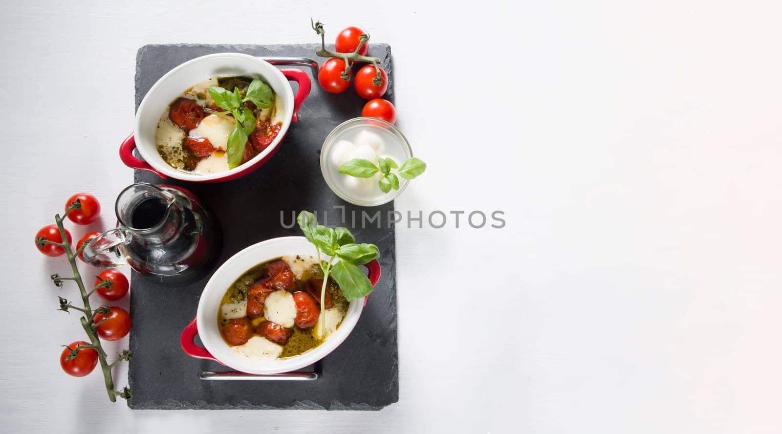 Italian caprese salad, baked cherry tomatoes, mozzarella and basil on a white table, still life, flat lay, copy space