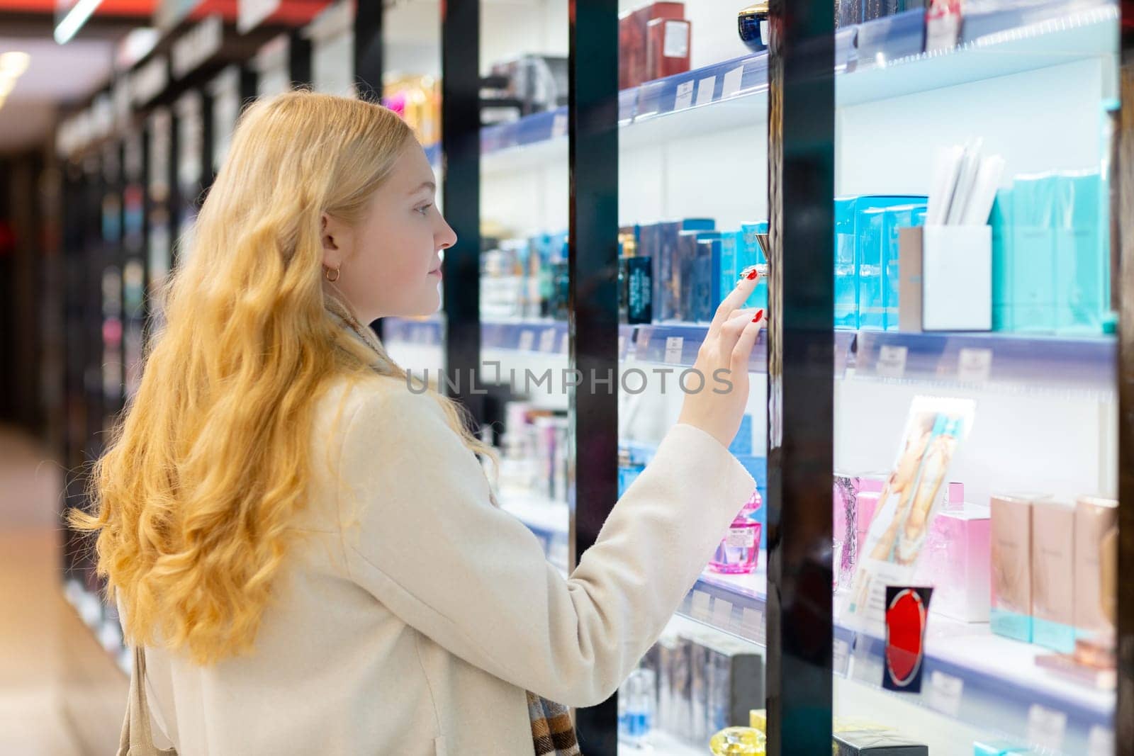 Beautiful young woman with long golden hair choosing perfume in shop. by BY-_-BY