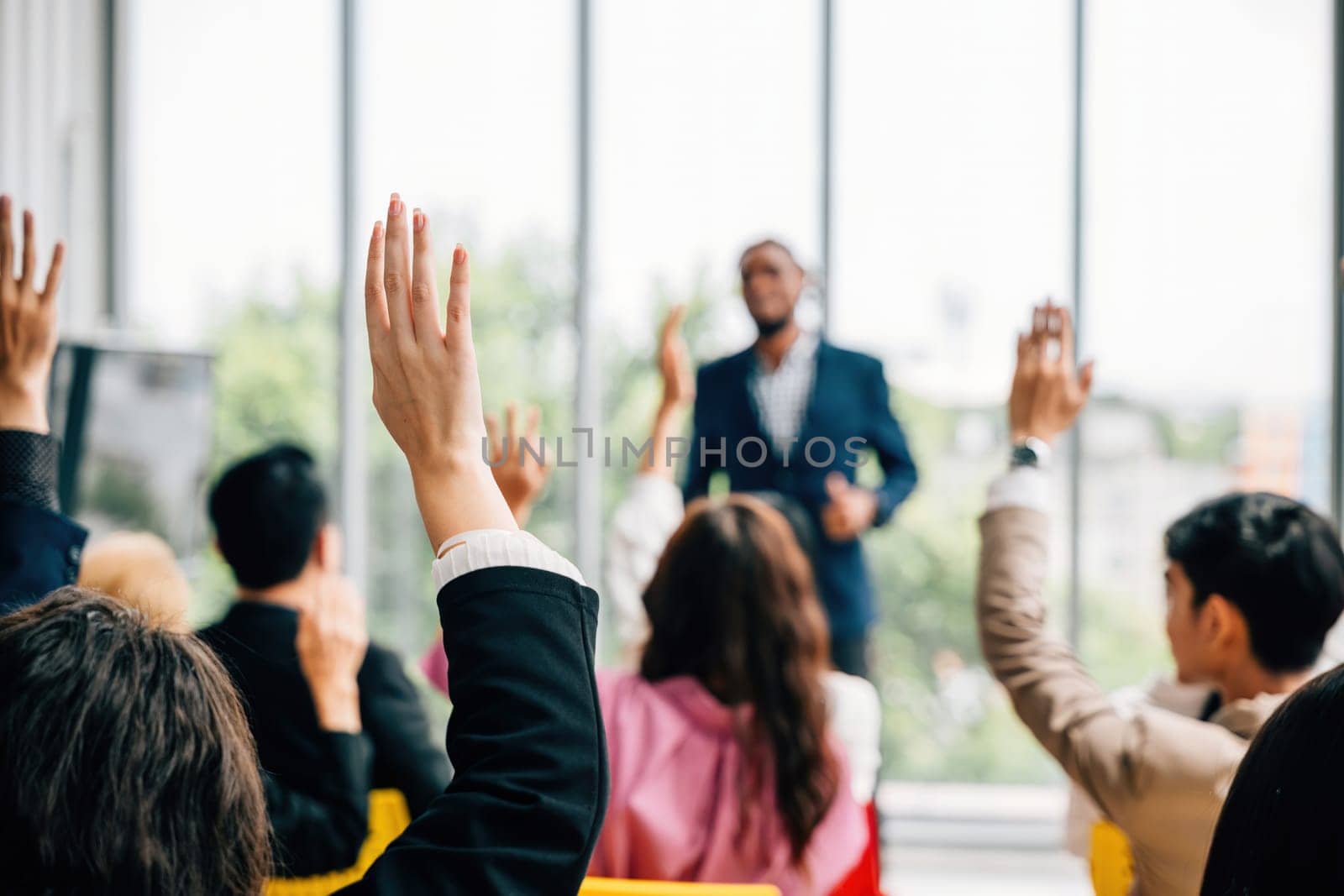 In a conference and convention at a corporate event businesspeople raise their hands to ask questions and vote. The meeting training seminar and discussions emphasize teamwork and collaboration. by Sorapop