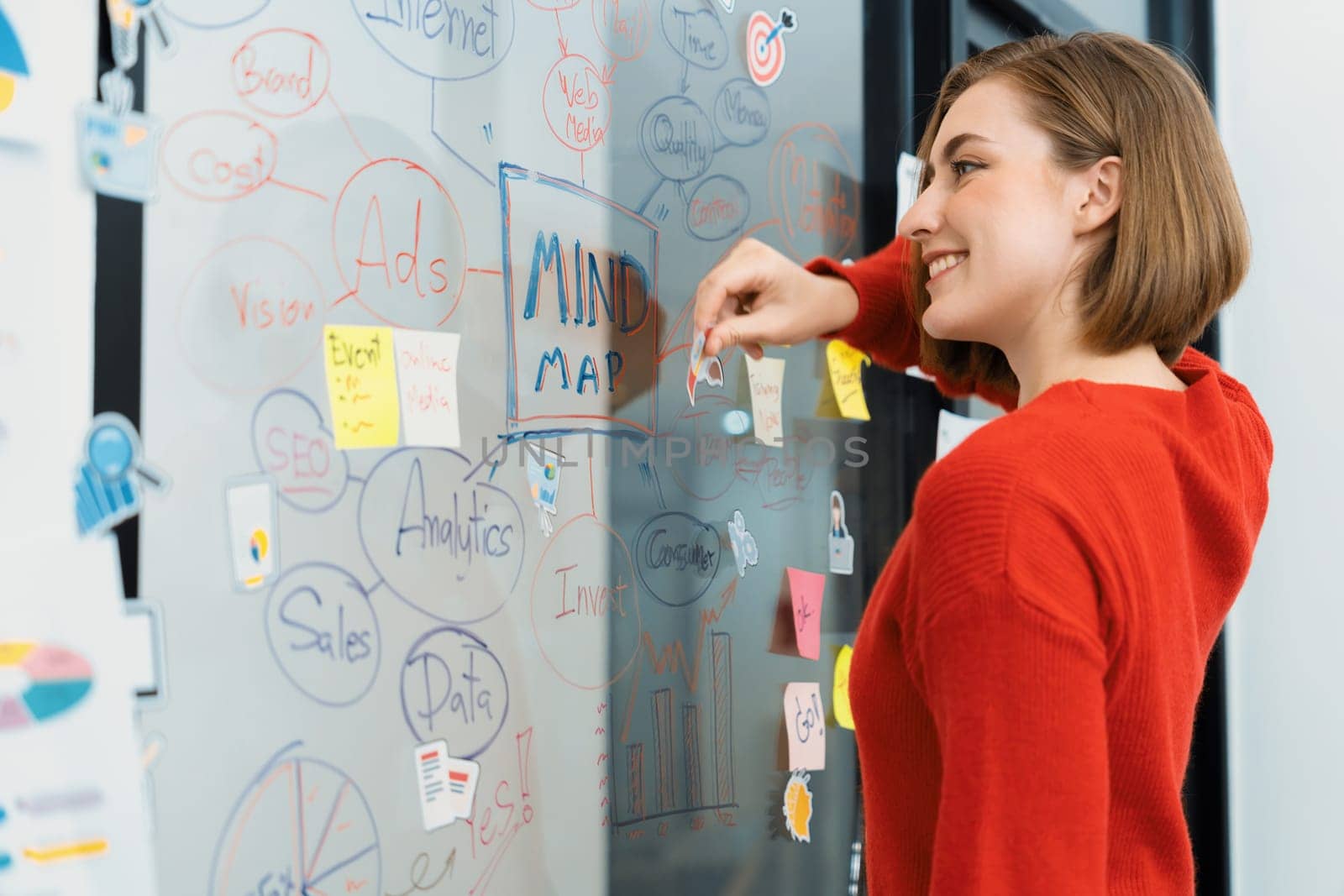 Professional attractive female leader sticks sticky note while presents creative marketing plan by using brainstorming mind mapping statistic graph at modern business meeting room. Immaculate.