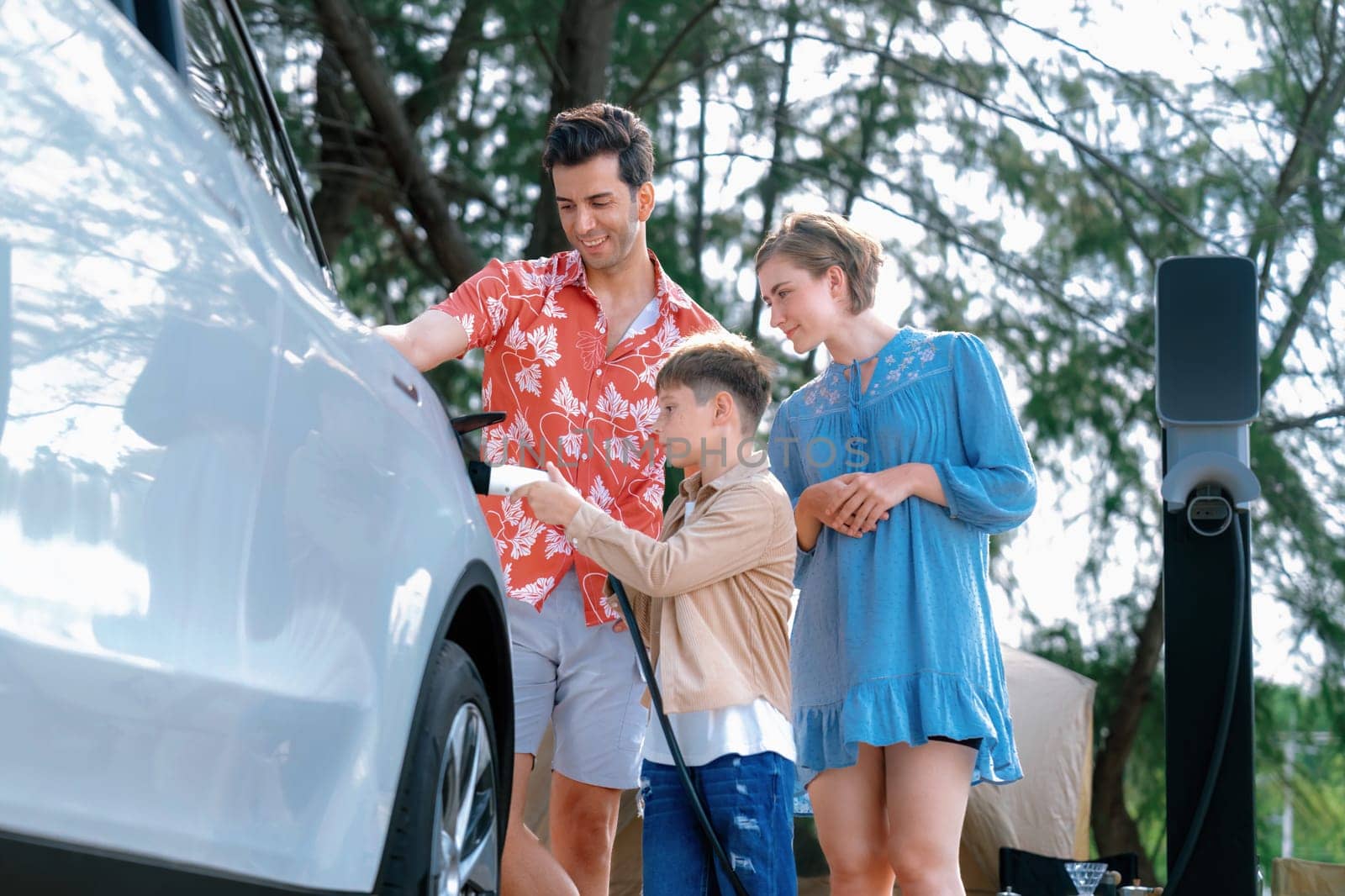 Outdoor adventure and family vacation camping in nature travel by eco friendly car for sustainable future. Lovely family recharge EV car with EV charging station in campsite. Perpetual