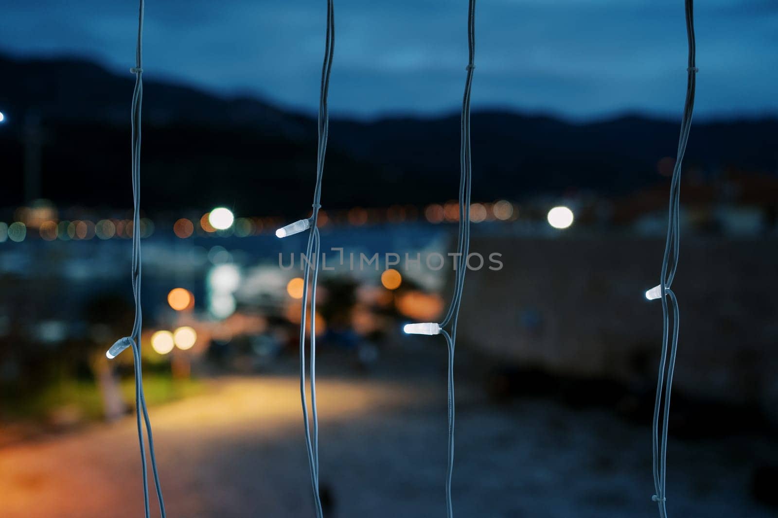 Vertical rows of luminous garlands against the background of a dark city and mountains. High quality photo