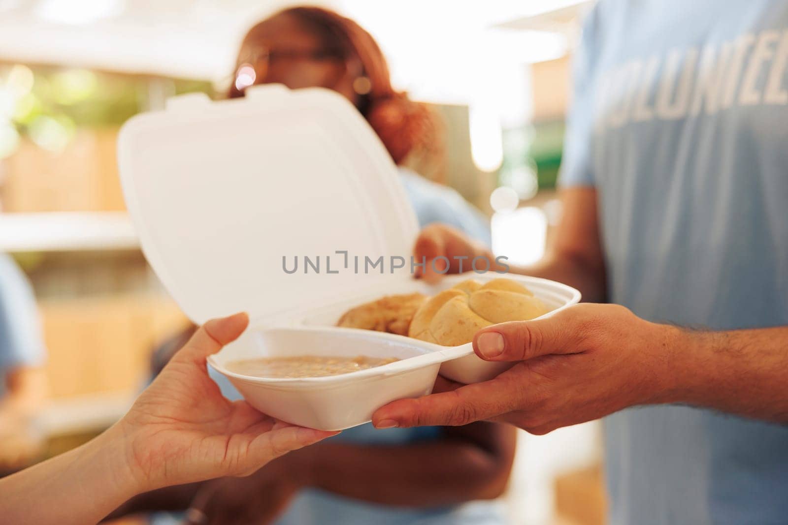 Detailed view of less fortunate woman receiving free food from male volunteer at outdoor food bank. Close-up of a pair of caucasian hands holding meal box donation for the hungry and homeless people.