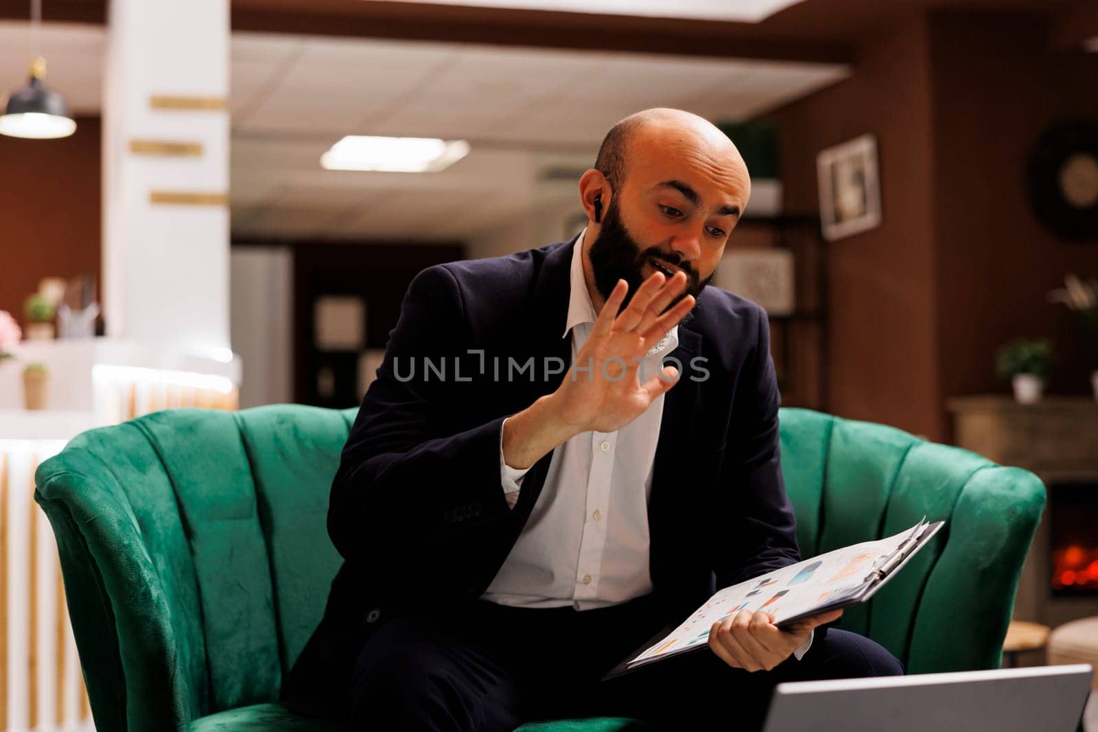 Businessman attends videocall in hotel lobby, killing time while he waits to check in. Entrepreneur in suit using laptop to meet online with manager, videoconference telework in lounge area.