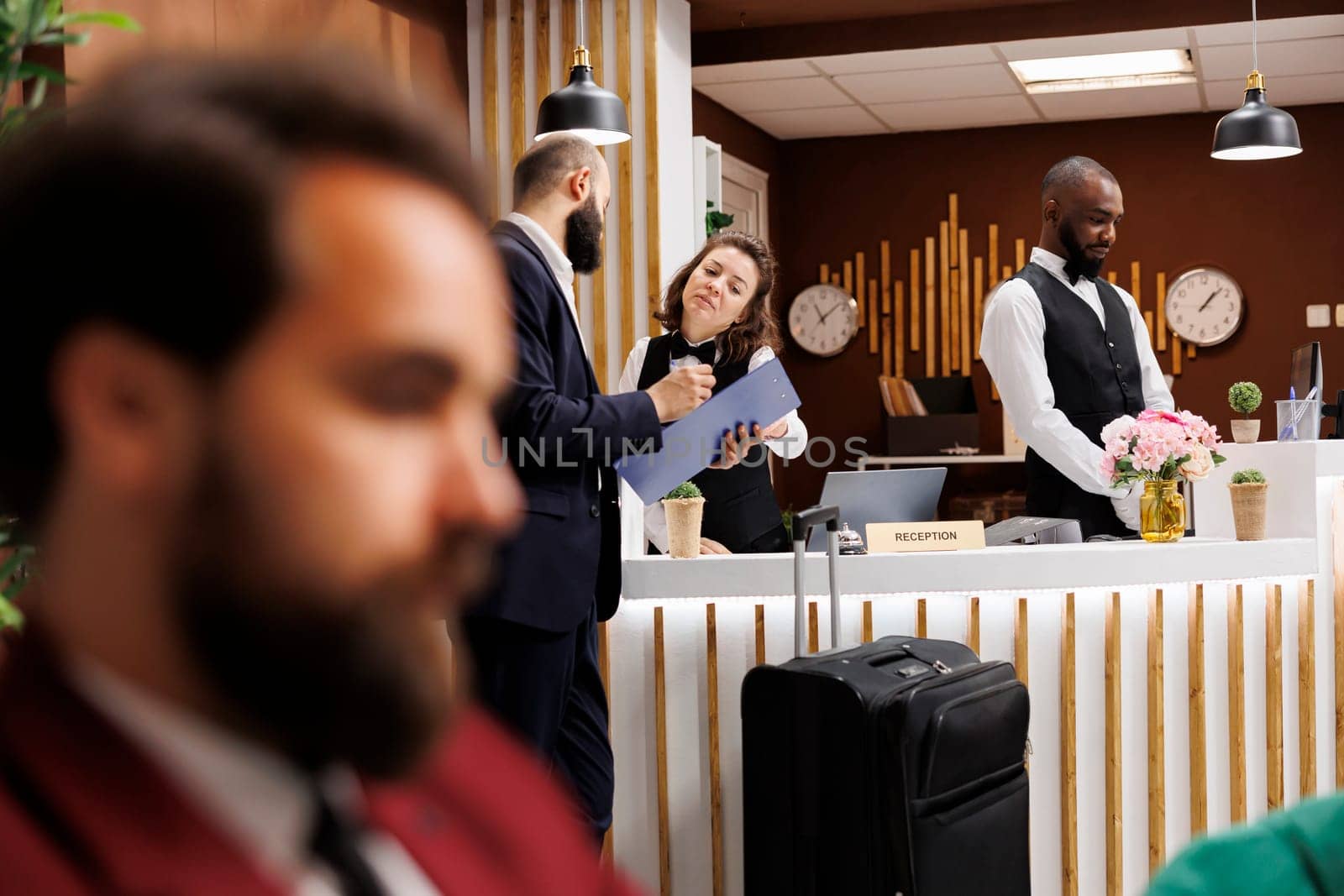 Hotel receptionist doing check in for businessman at front desk, providing luxury concierge services to guest. Client signing papers and travelling for work business meetings abroad.