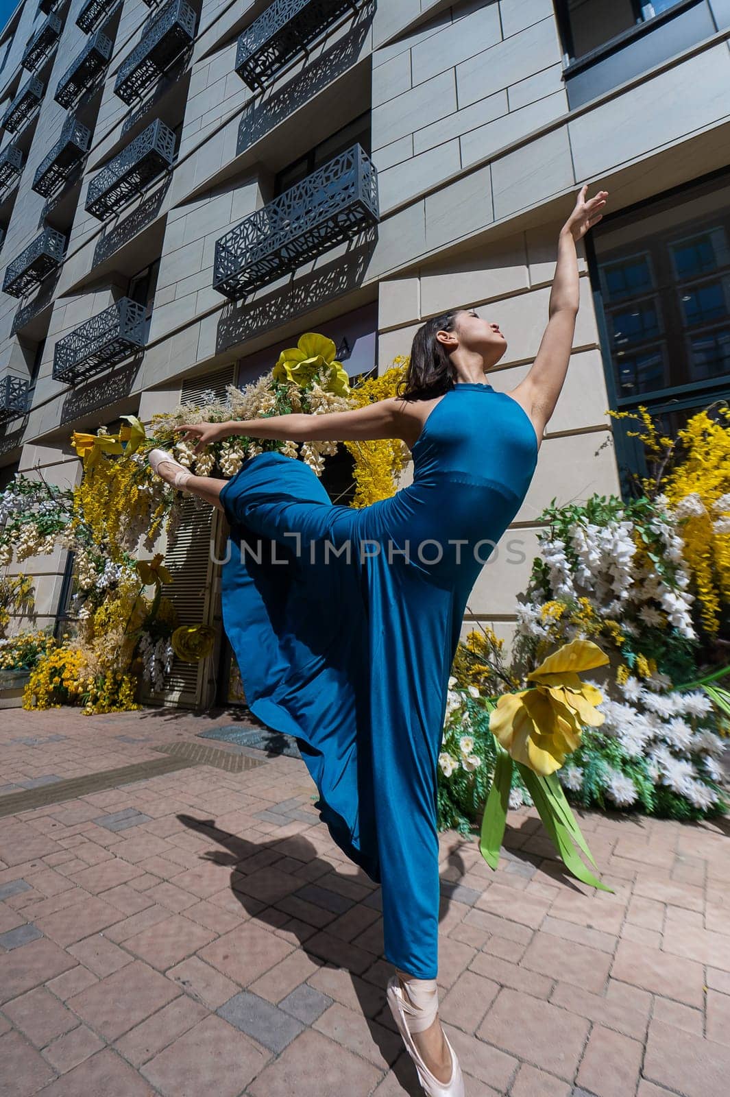 Beautiful Asian ballerina dances against the background of a building decorated with flowers. Vertical photo