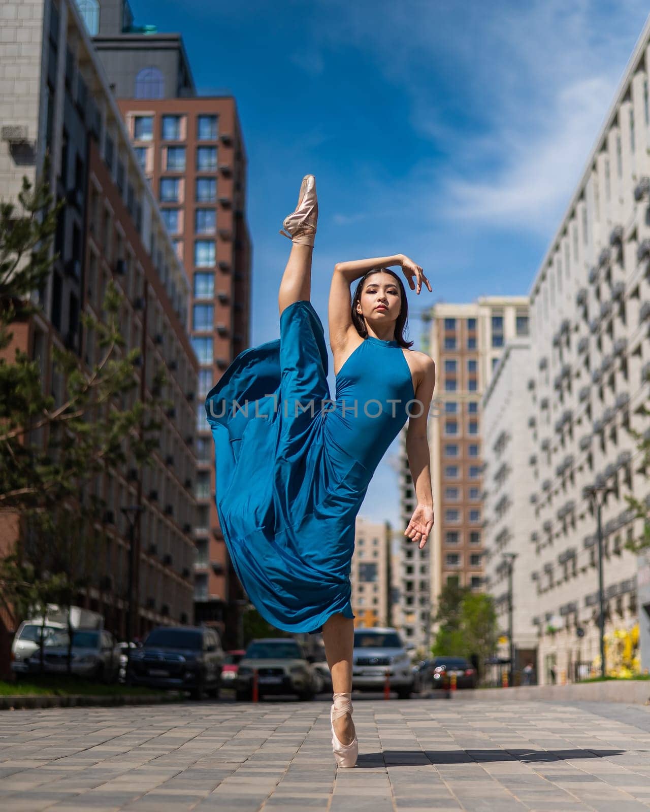 Beautiful Asian ballerina in blue dress posing in splits outdoors. Urban landscape. Vertical photo. by mrwed54