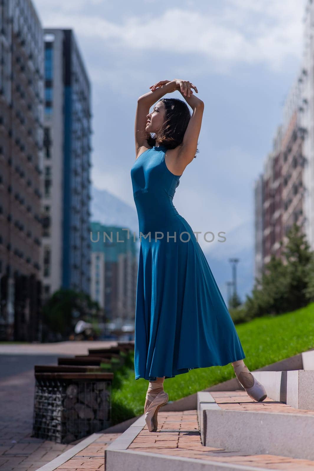 Beautiful Asian ballerina in blue dress posing on stairs outdoors. Urban landscape