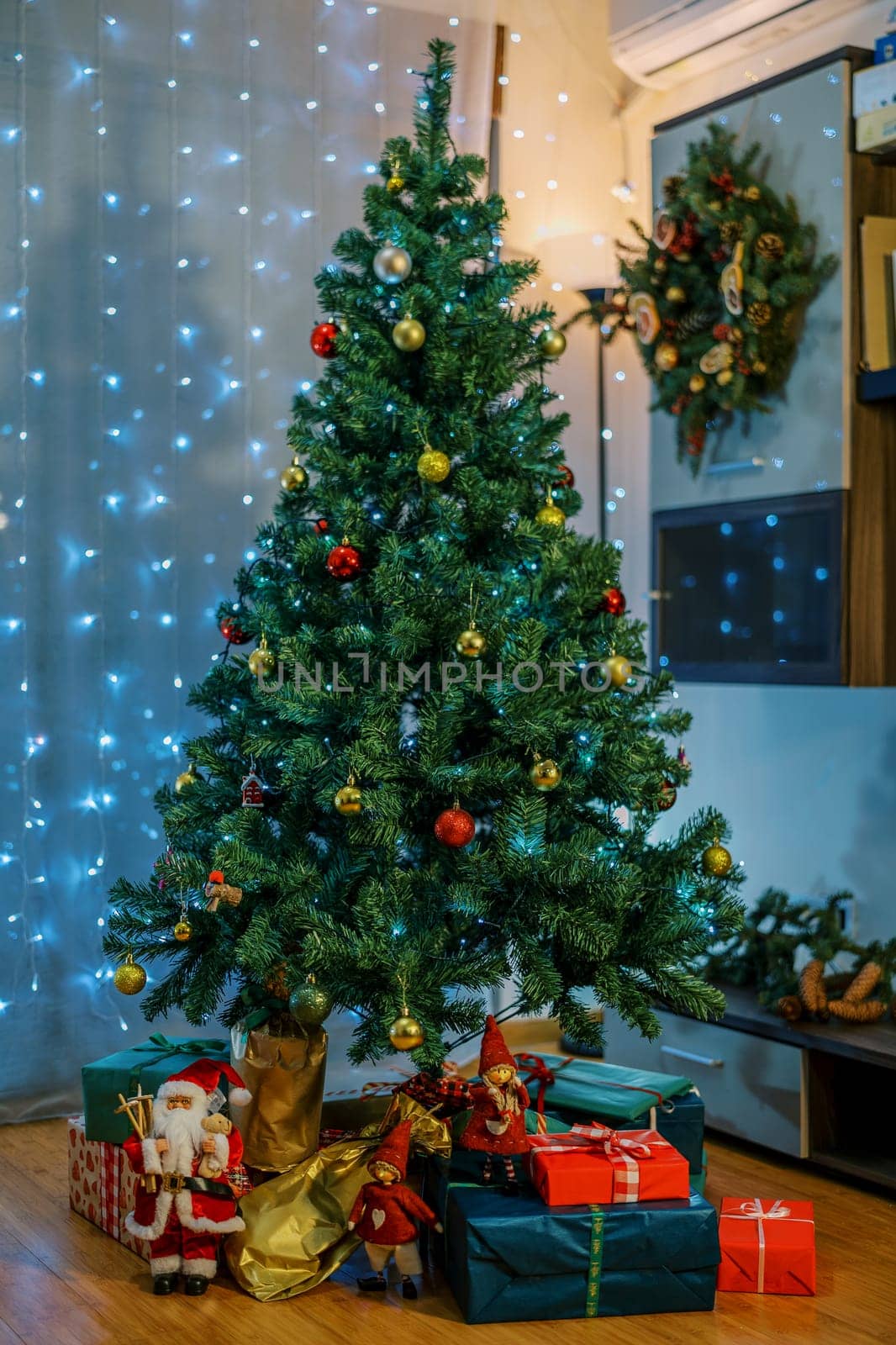 Figurines of Santa and gnomes stand on colorful gifts lying under the Christmas tree in the room. High quality photo