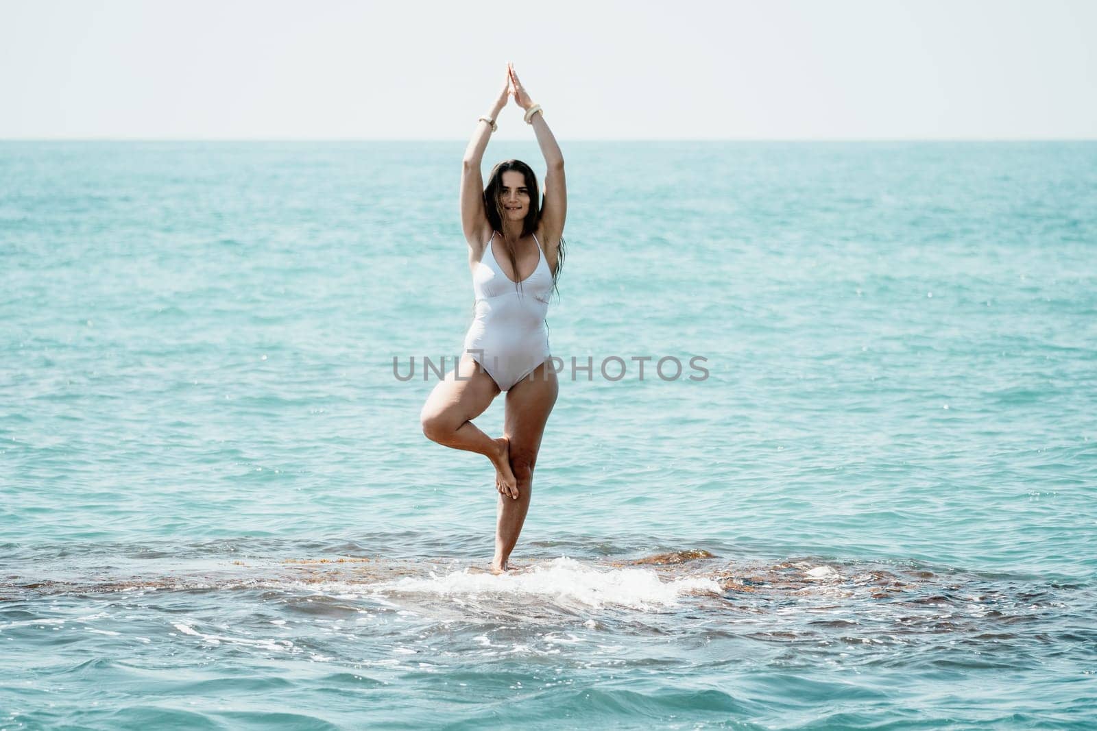 Woman sea yoga. Back view of free calm happy satisfied woman with long hair standing on top rock with yoga position against of sky by the sea. Healthy lifestyle outdoors in nature, fitness concept by panophotograph