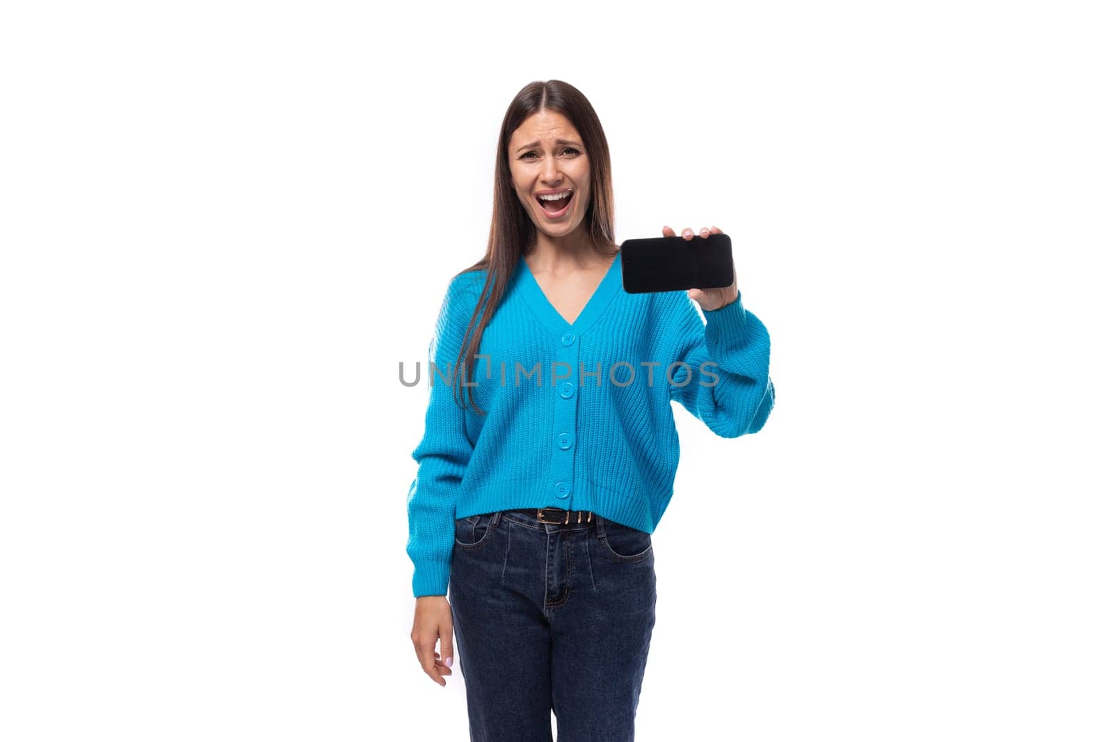 charming caucasian woman with black hair dressed in a blue cardigan shows the smartphone screen forward with a mockup for advertising. e-business concept.