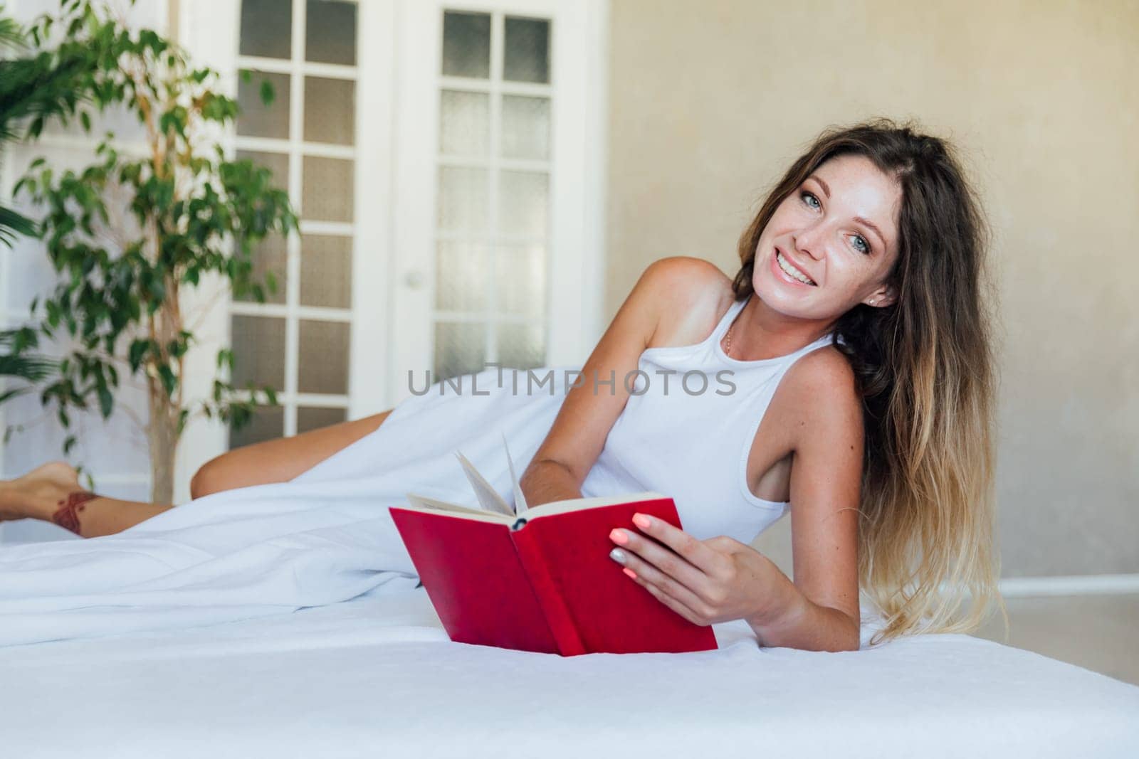 Beautiful woman in pajamas reading a book in the bedroom on the bed