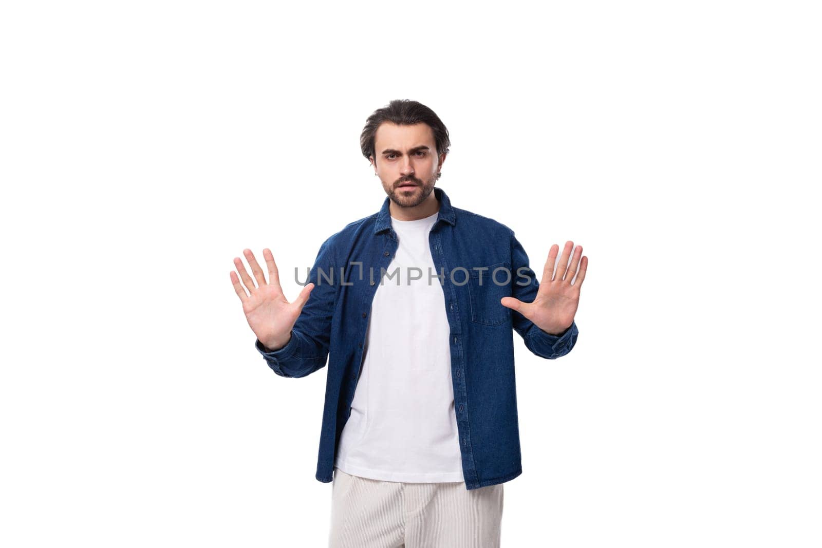 young serious handsome brutal brunette guy in a denim shirt and light-colored trousers.