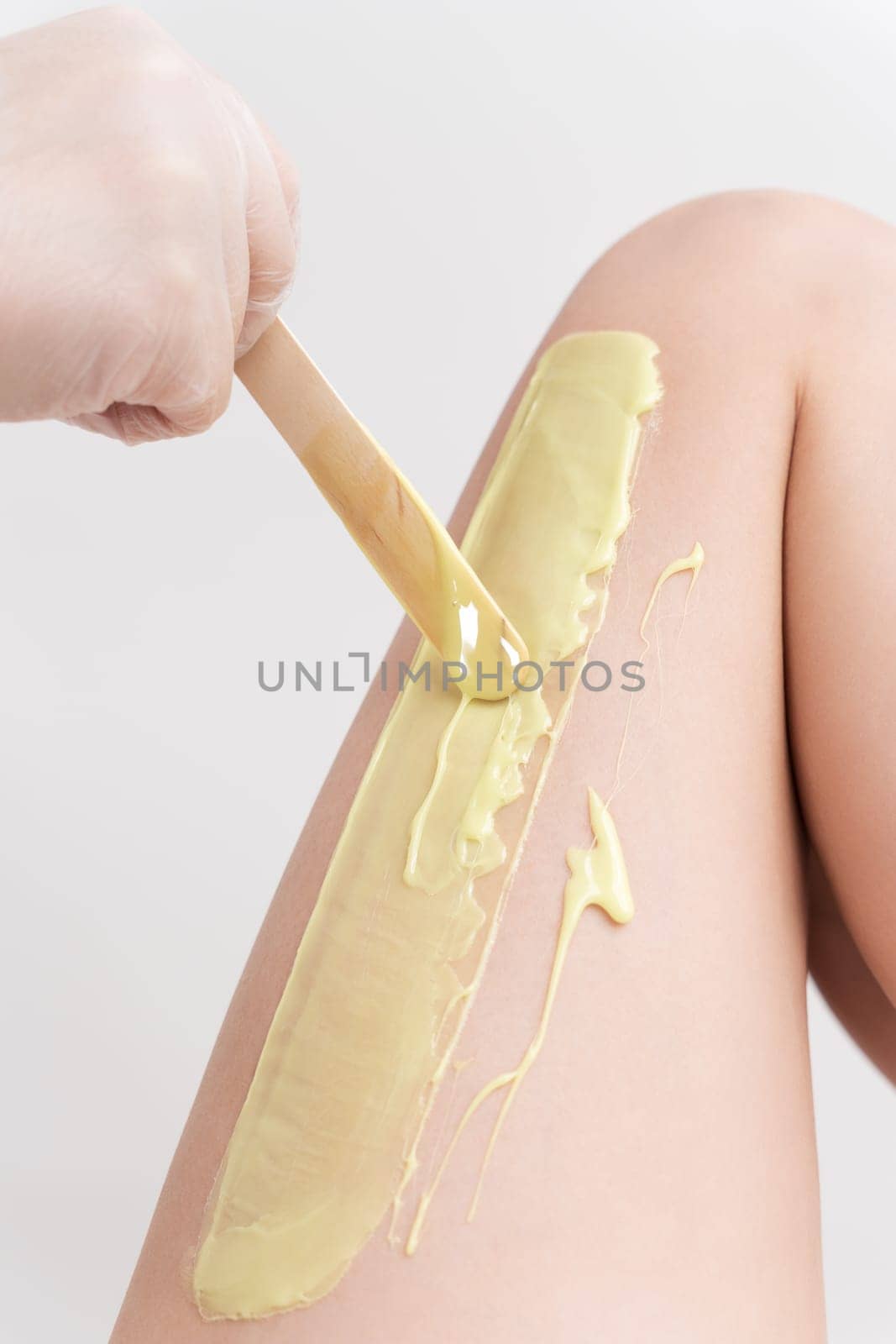 Closeup hand in glove applying hot wax on woman leg using spatula. Professional depilation procedure by Alexander-Piragis