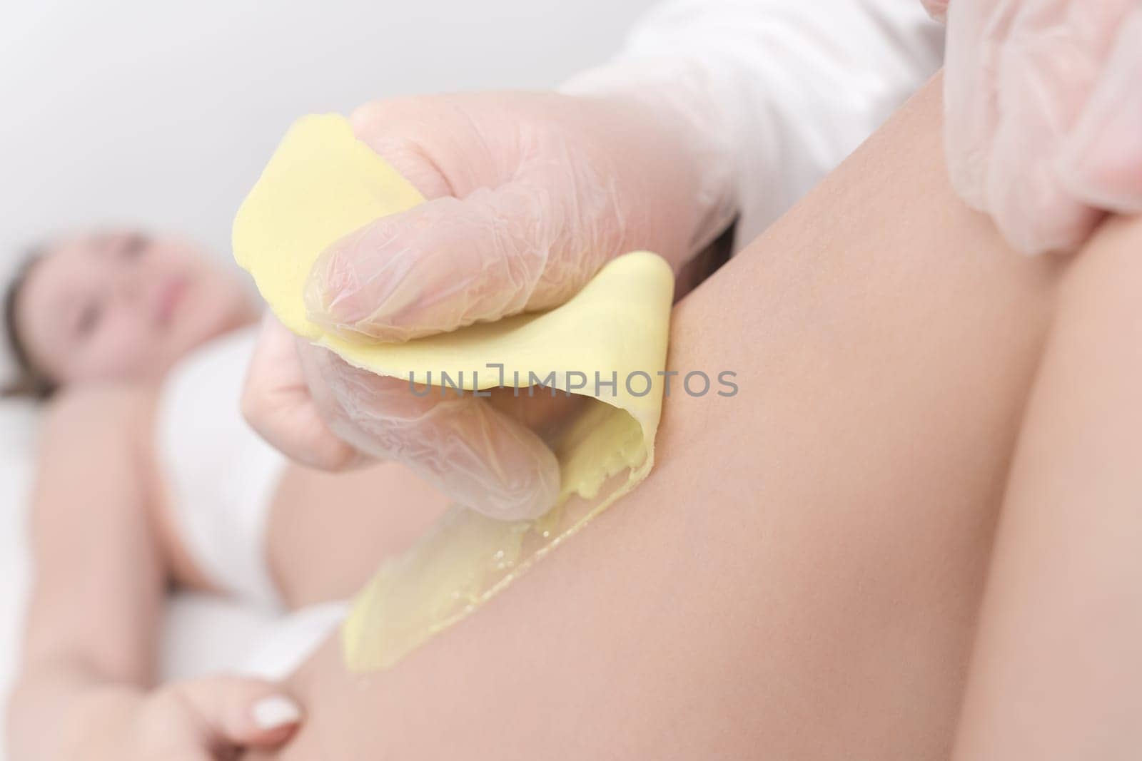 Waxing process - closeup view of quick sudden movement of cloth with green hot wax in professional beauty salon. Cosmetologist removing hair on women leg. Part of photo series.