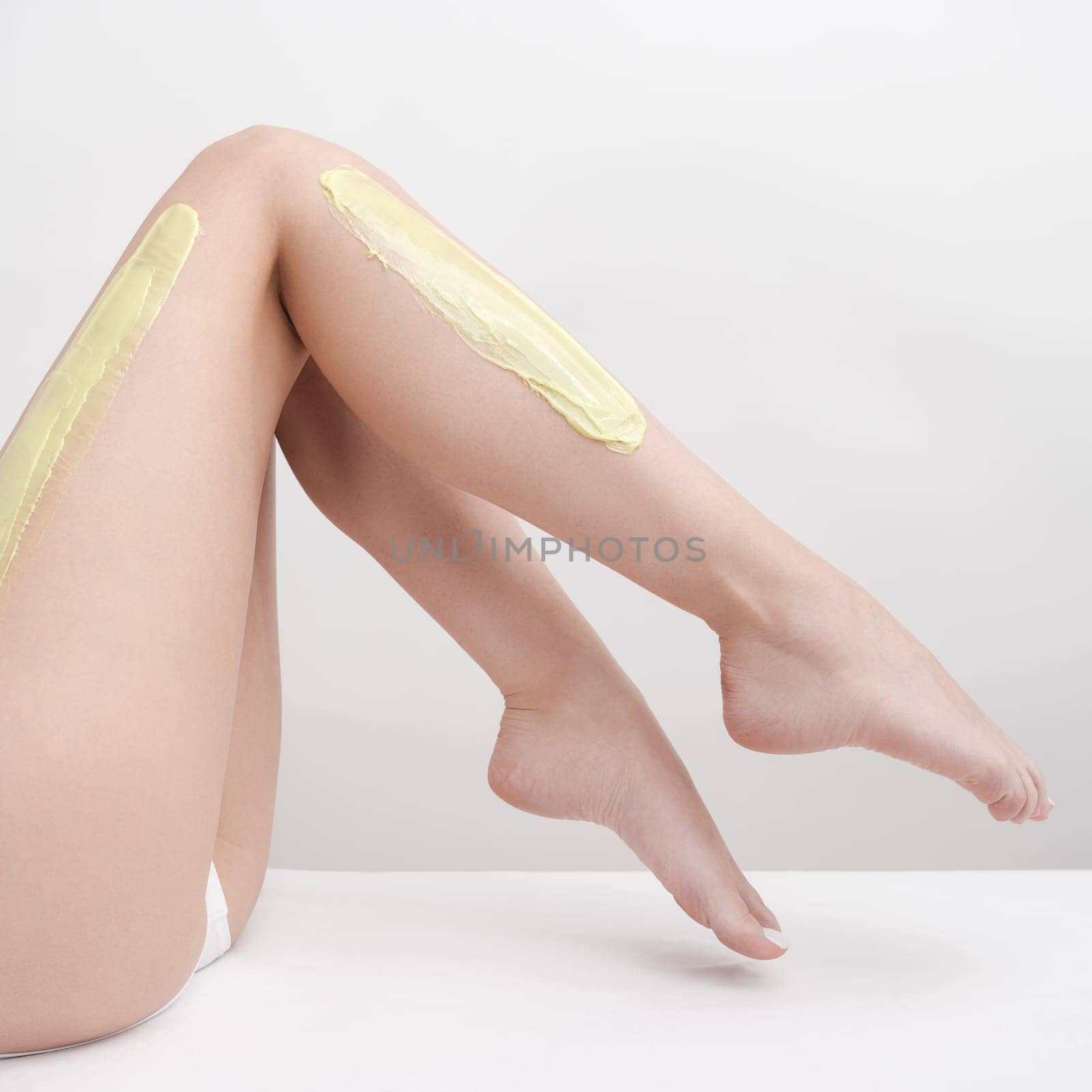 Beautiful legs of slim woman while she lying down on couch during depilation process with green hot wax in professional beauty salon. Side view of body in white panties. Part of photo series.