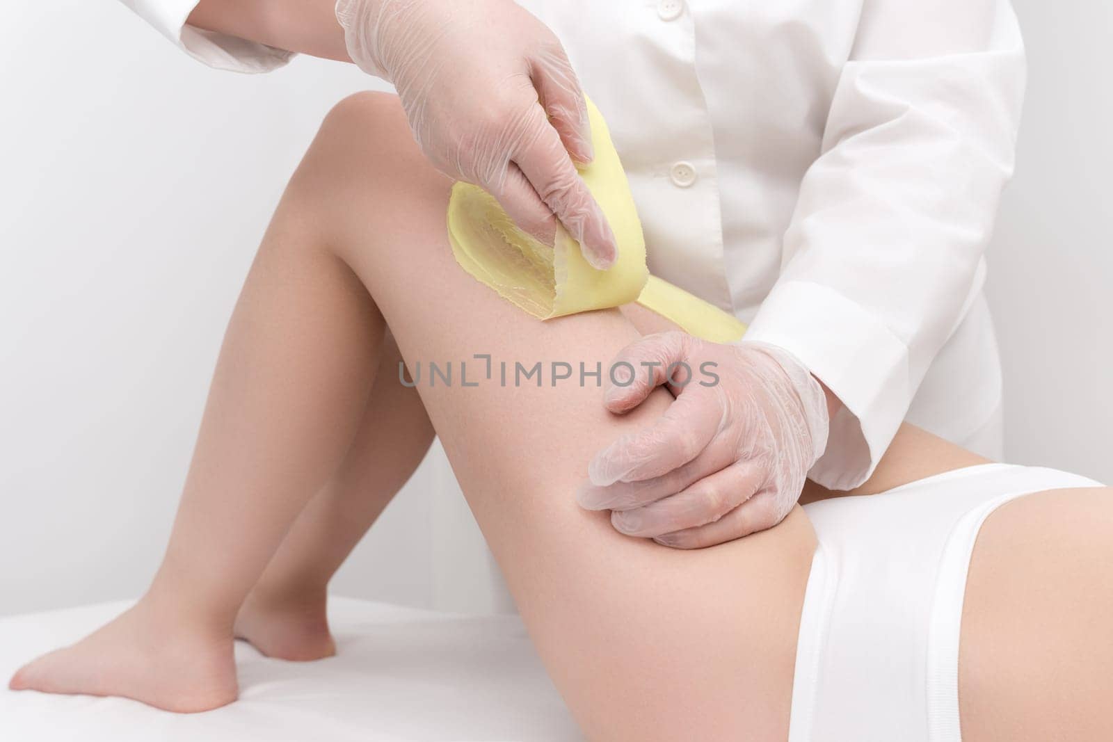 Cosmetologist hands in gloves removing hair on women leg. Depilation procedure with green hot wax in professional beauty salon. Part of photo series.