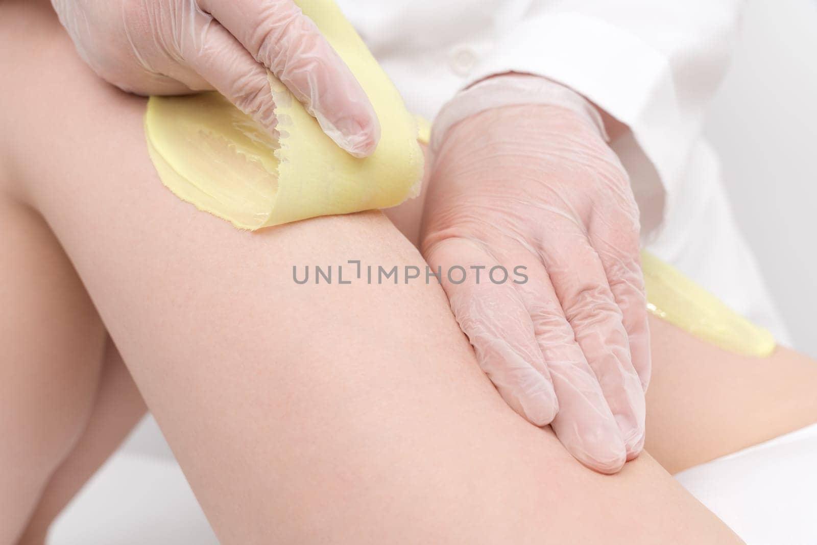 Closeup of cosmetologist hands doing depilation to woman legs with green hot wax in beauty salon. Waxing process of hair removal from root. Women intimate hygiene concepts. Part of photo series.