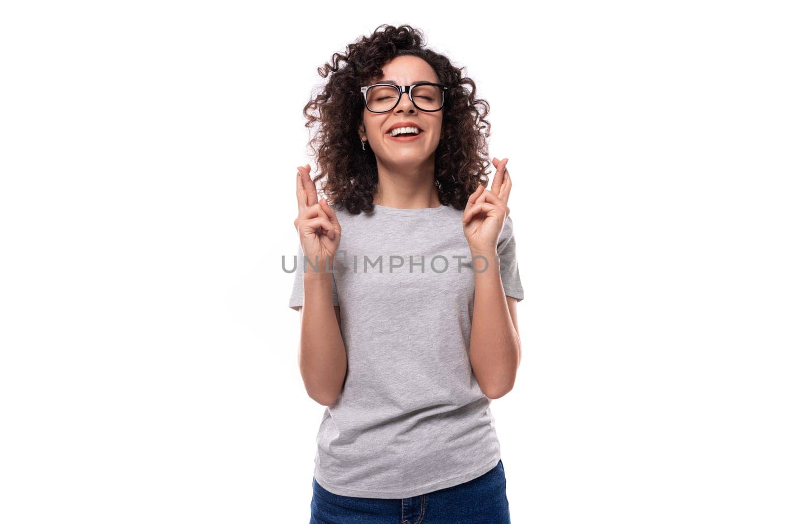 hopeful curly brunette promoter woman with glasses wearing a gray t-shirt crossed her fingers.