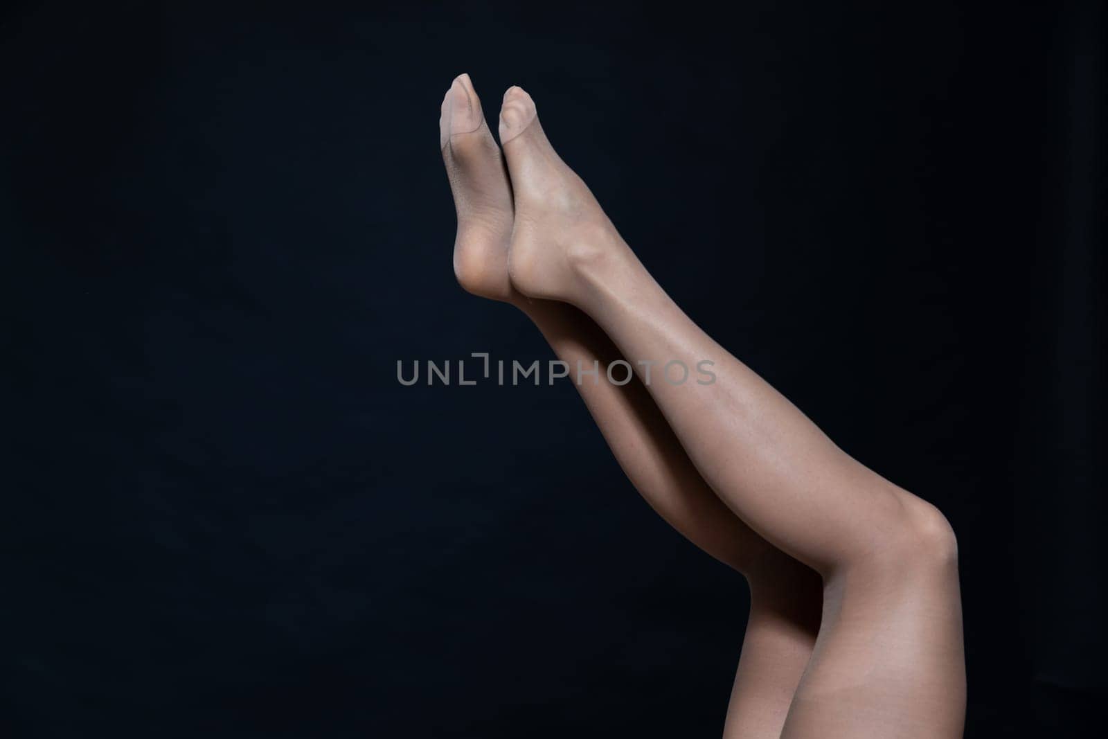 a women's slender legs in brown tights on a black background