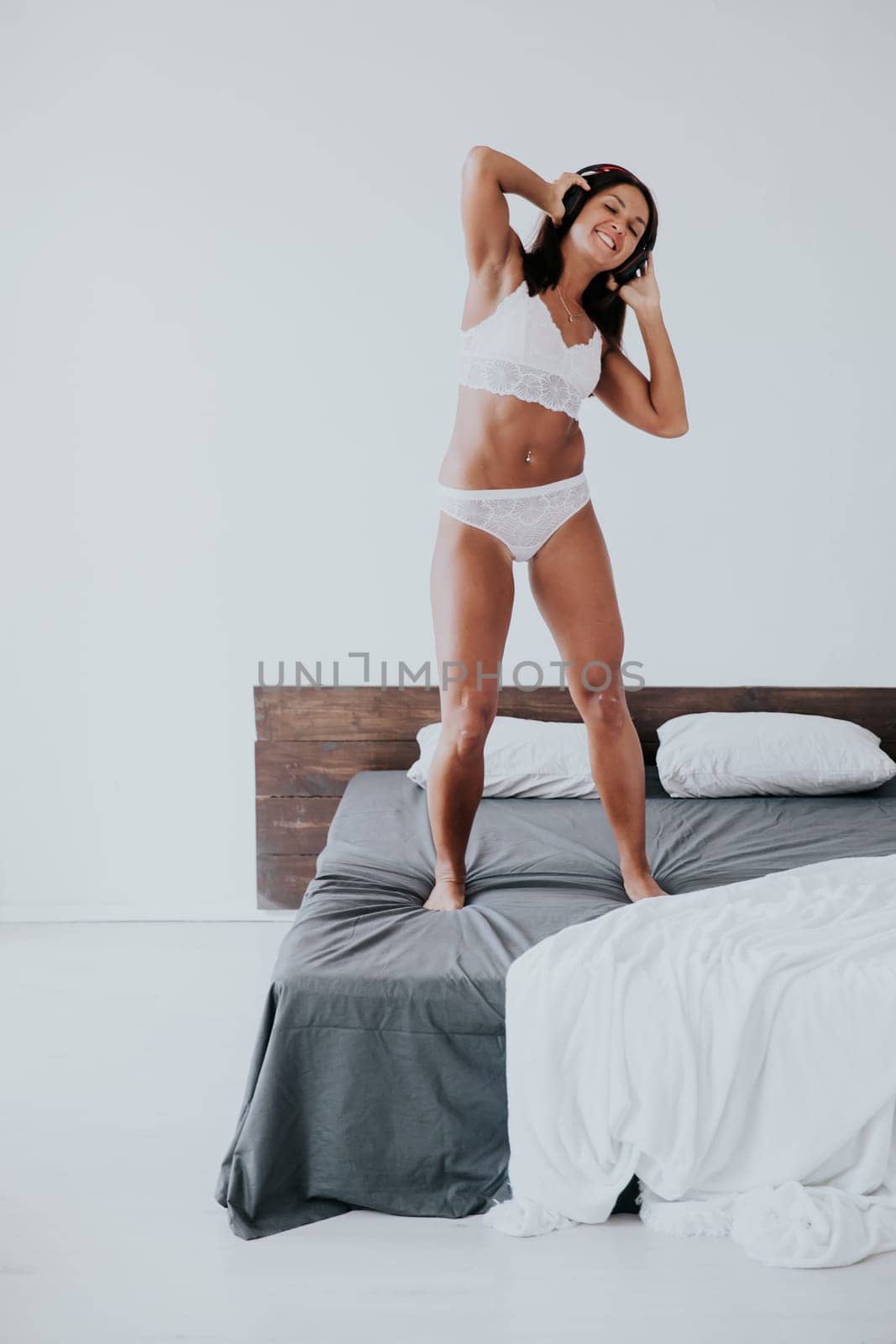 woman in underwear with headphones standing on the bed and listening to music dancing