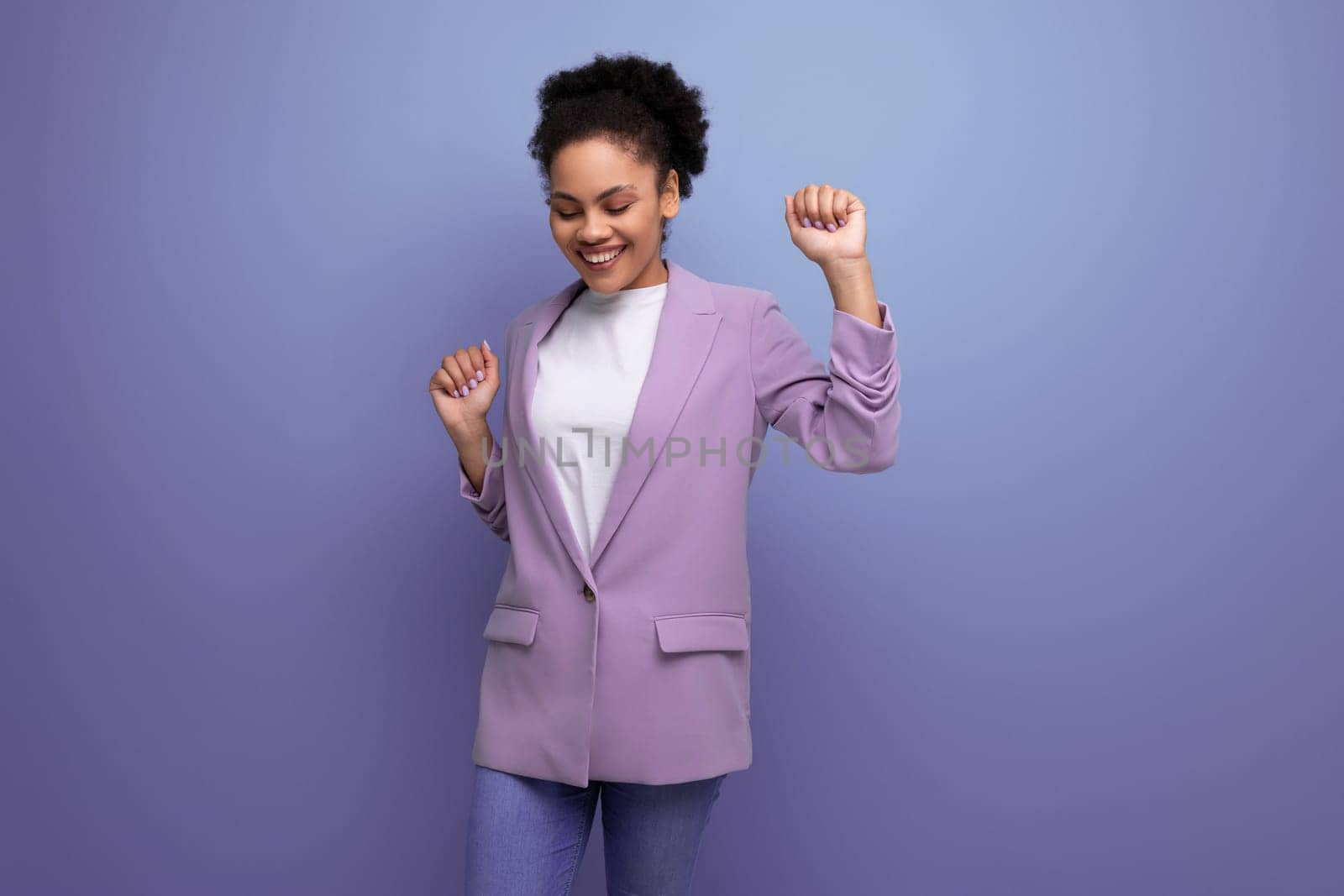 young well-groomed latin secretary woman with fluffy hair is dressed in a lilac jacket on a studio background with copy space.