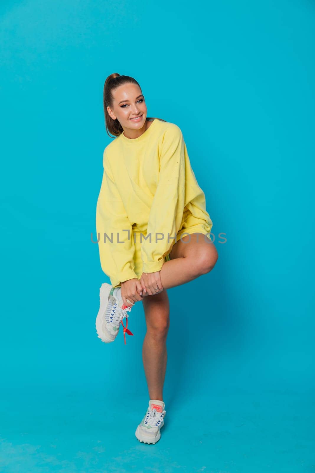 a woman in a tracksuit and sneakers holds a leg by Simakov