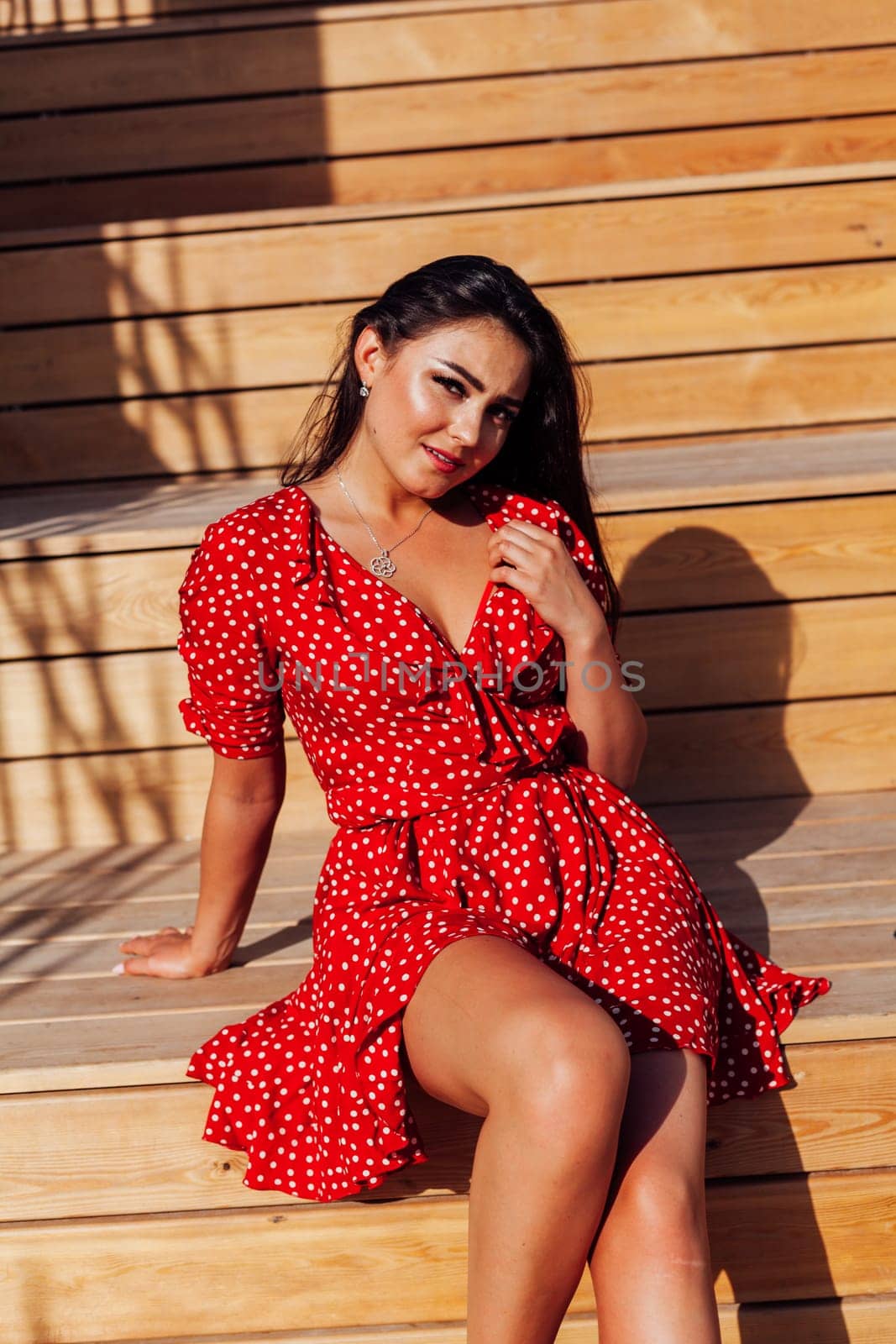 brunette woman in a red dress sits on wooden steps