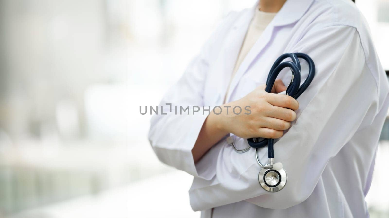 Cropped shot of an unrecognizable doctor standing with arms folded isolated on clear white hopital hall background. Copy space. medicine doctor holding stethoscope in hand wearing medical gown standing