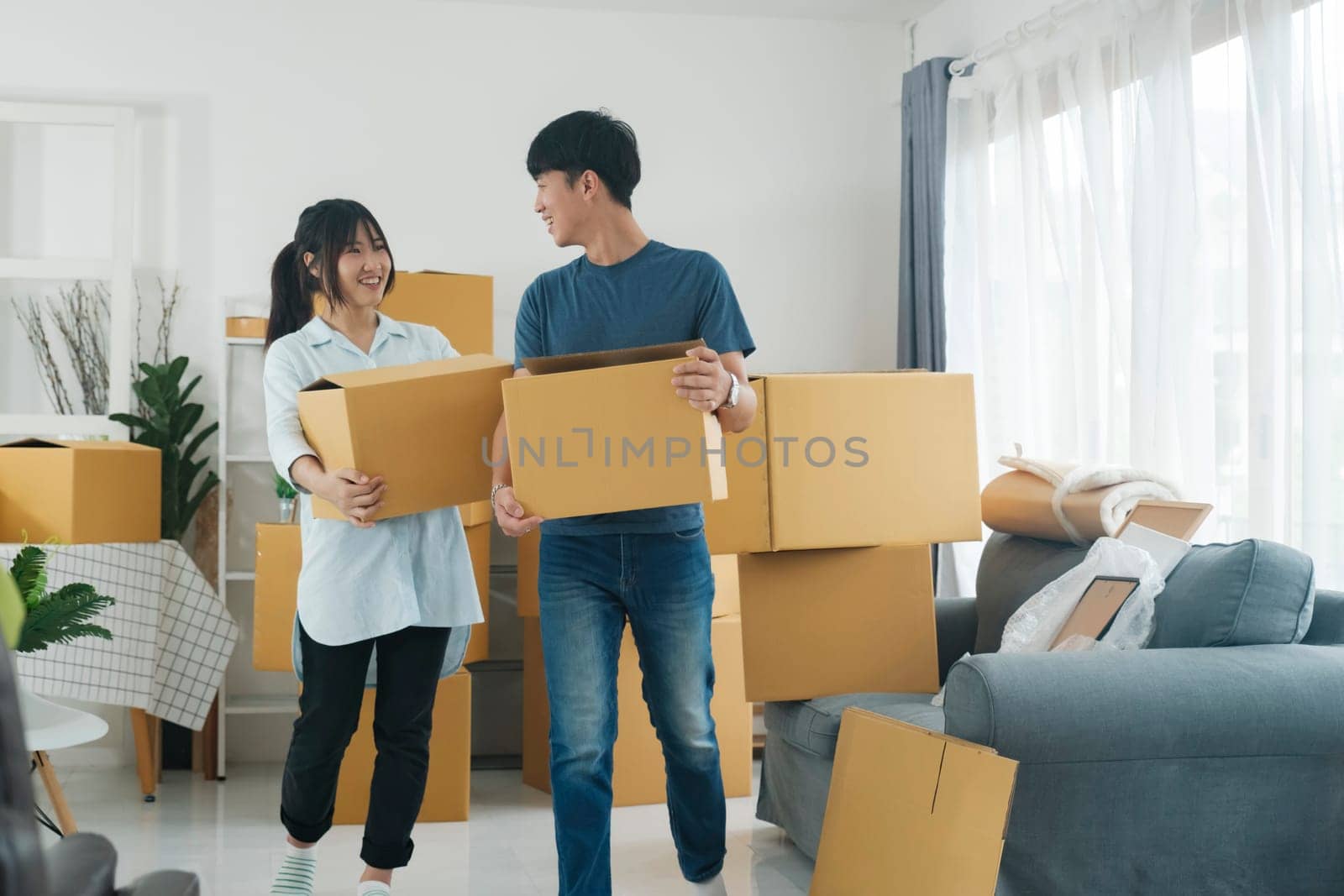 Asian young happy new married couple moving to their new house or real estate. An attractive romantic man and woman carry boxes parcel with happiness and love. Family moving house relocation concept.