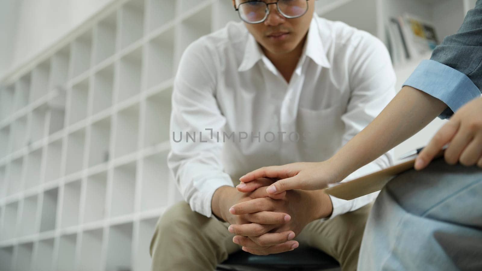 Psychiatrist or counselor holding the patient's hand to comfort and encourage. Young Asian female psychologist keeping hand of wrist of male patient sitting in front of her and sharing his problems.