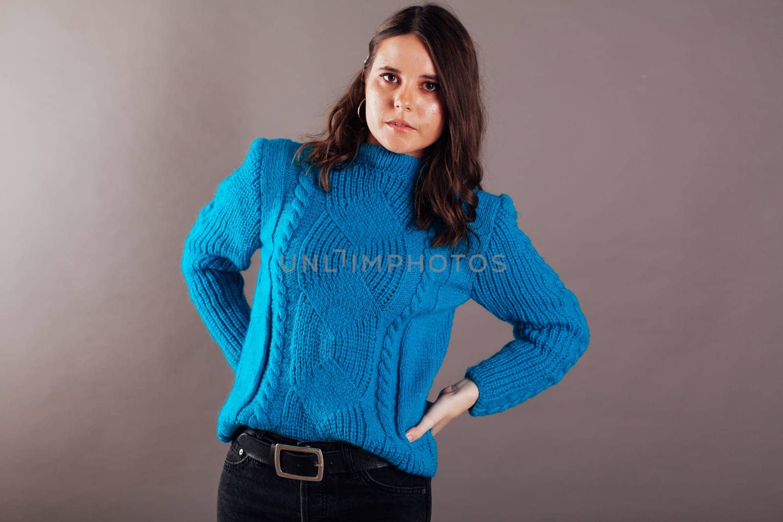 woman in a blue sweater poses on a gray background