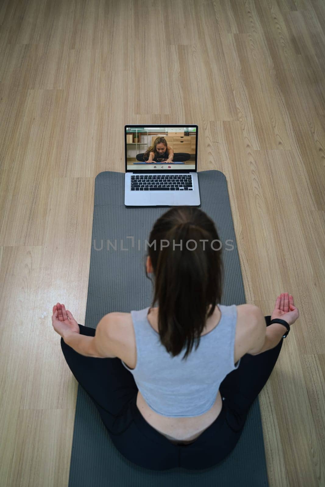 Above view of young woman doing yoga exercise and watching tutorial lesson on laptop at home by prathanchorruangsak