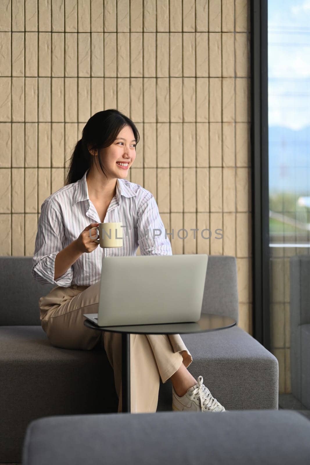Portrait of thoughtful young businesswoman holding a cup of coffee looking out of window.