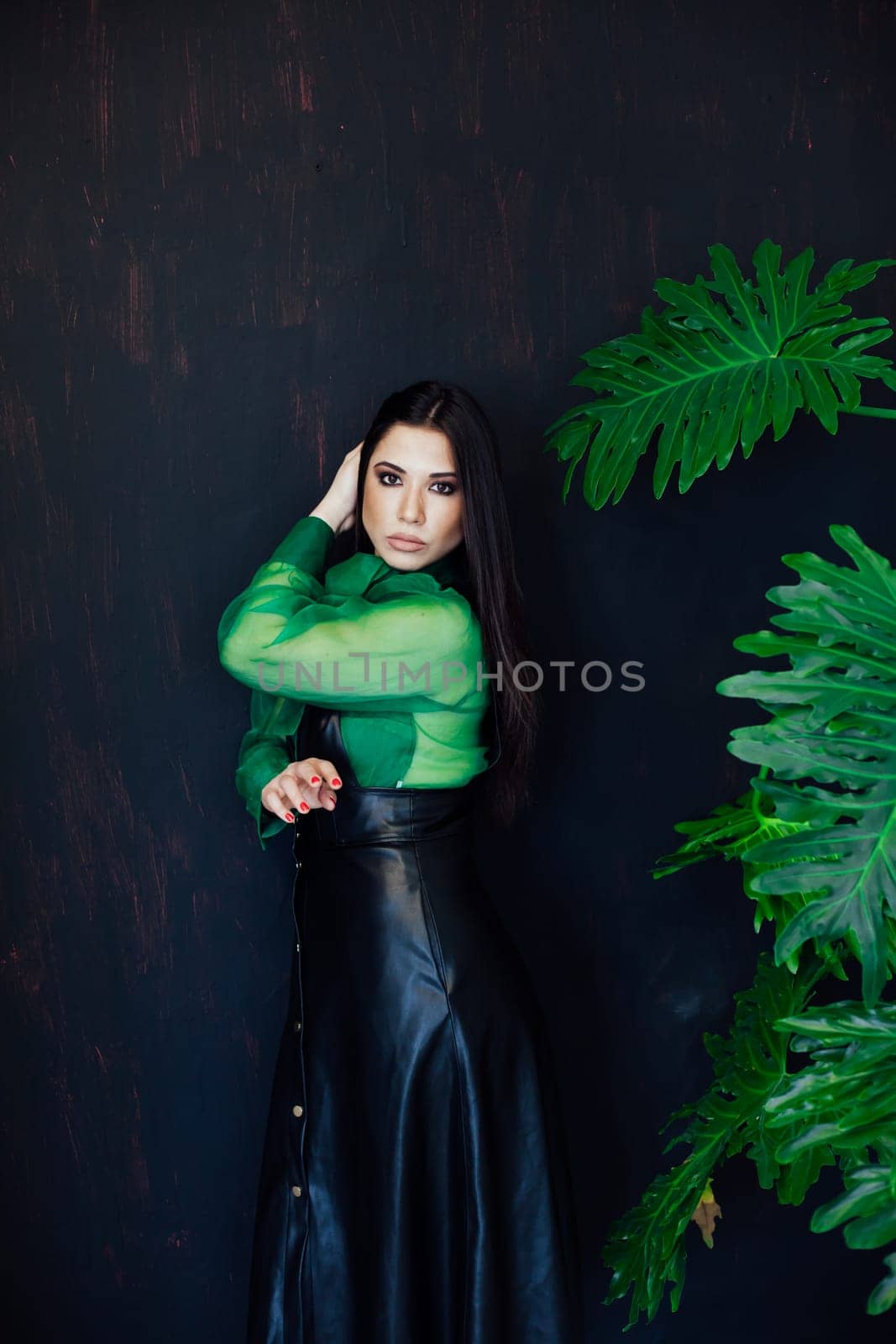 brunette in green shirt poses at a green plant on a black background