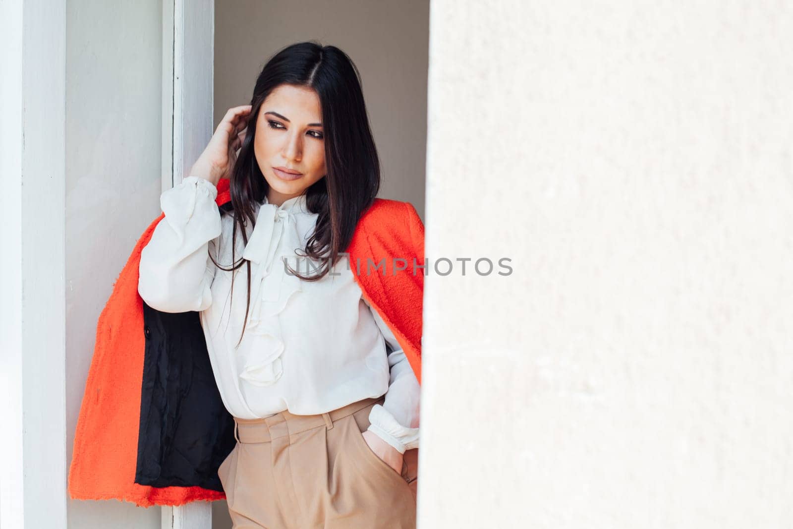 a woman fashionable brunette in a bright jacket business style in the office stands against the wall