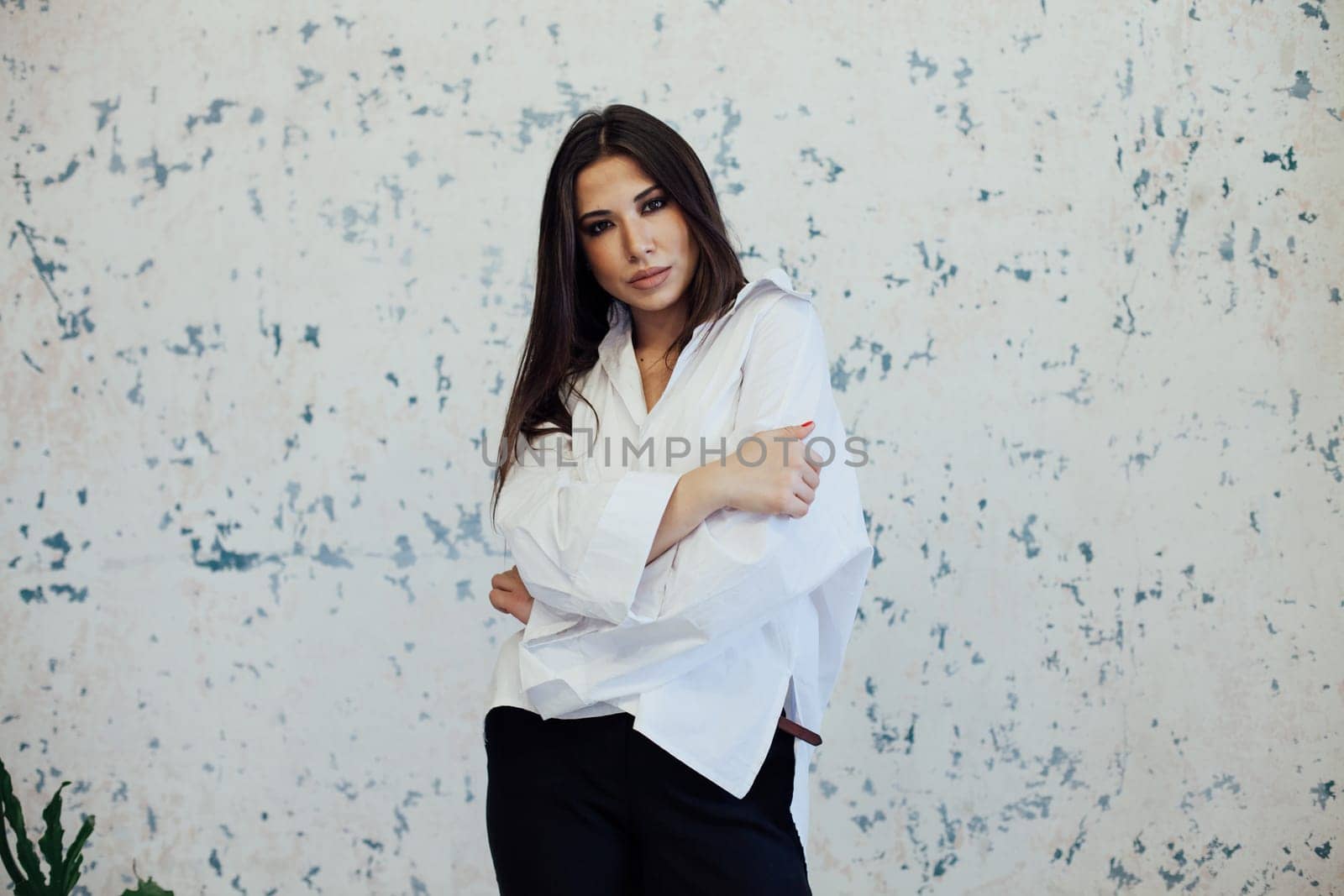 brunette woman in a white shirt posing against a textured wall