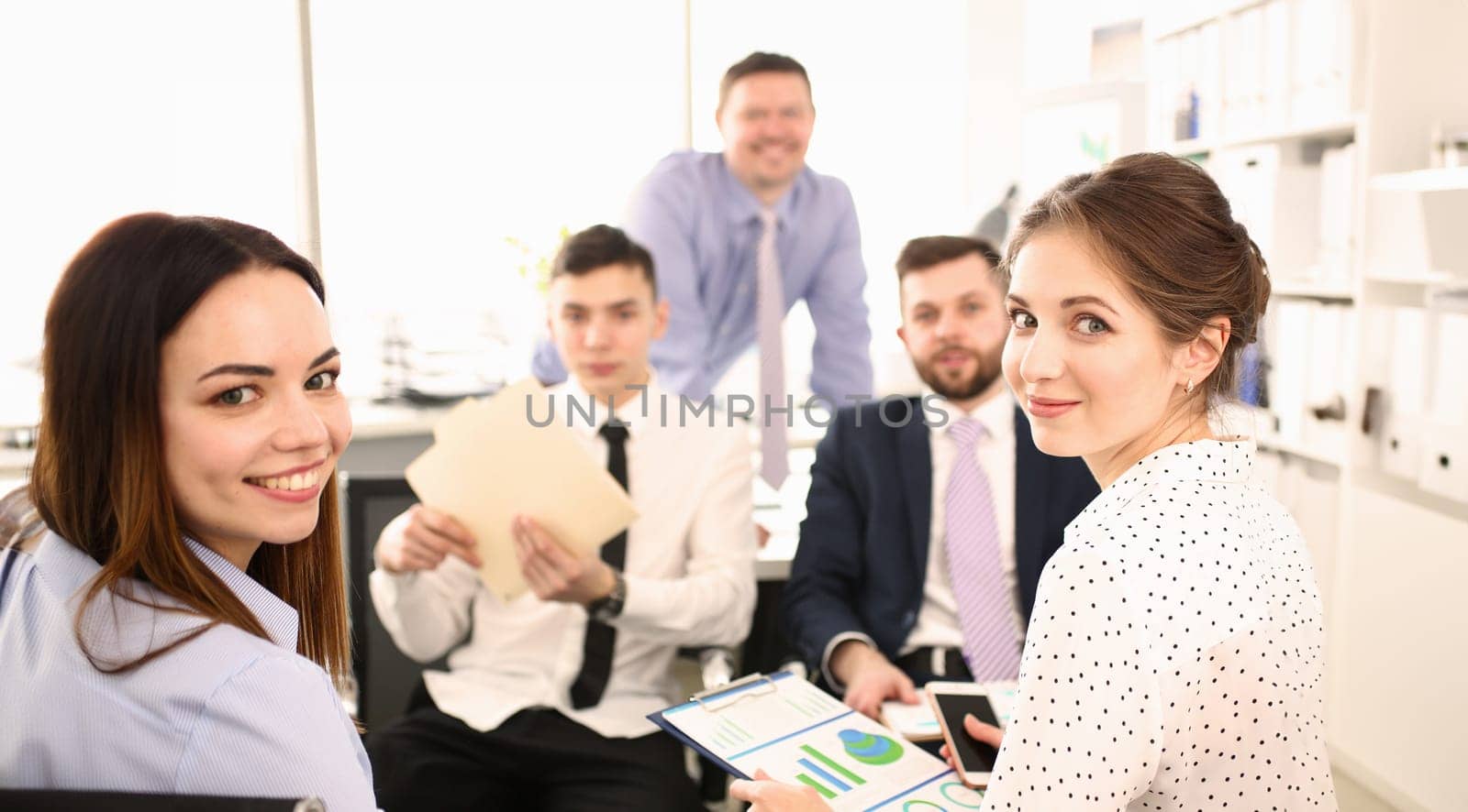 Portrait of biz people sitting in big modern office and looking at camera with joy. Woman holding paper folder with important documents that determine corporation future. Company meeting concept