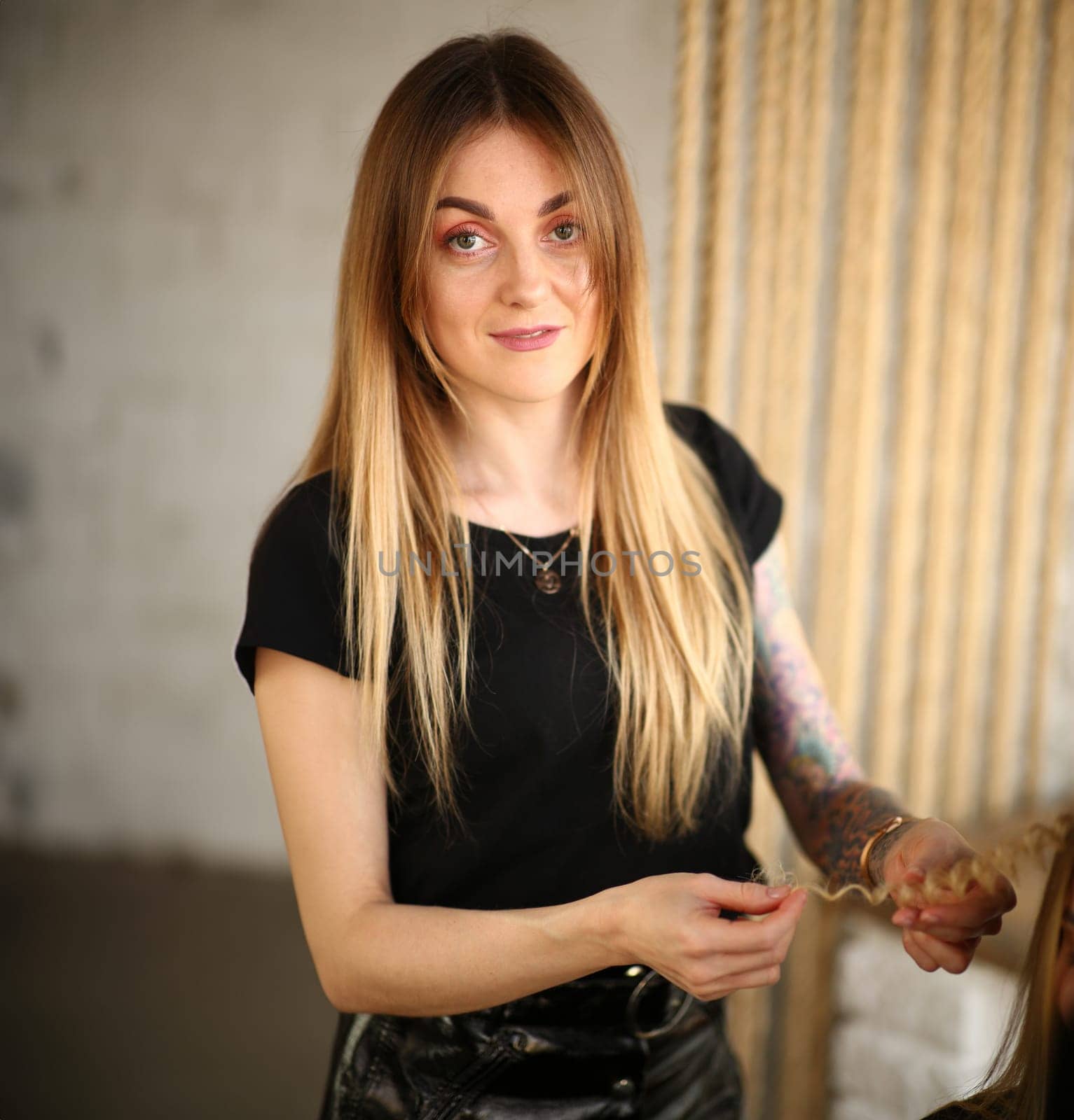 Woman Hairstylist Holding Curly Strand of Hair. Blonde Hairdresser Styling Curling Hairstyle. Beautiful Stylist Making Wavy Haircut. Professional Stylist Working in Studio Looking at Camera Shot