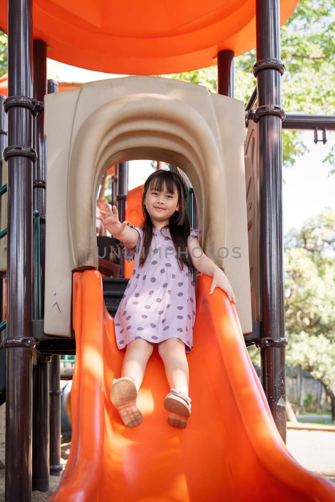 Asian little girl playing on the slider, Little pretty girl is while playing on the playground equipment in park.