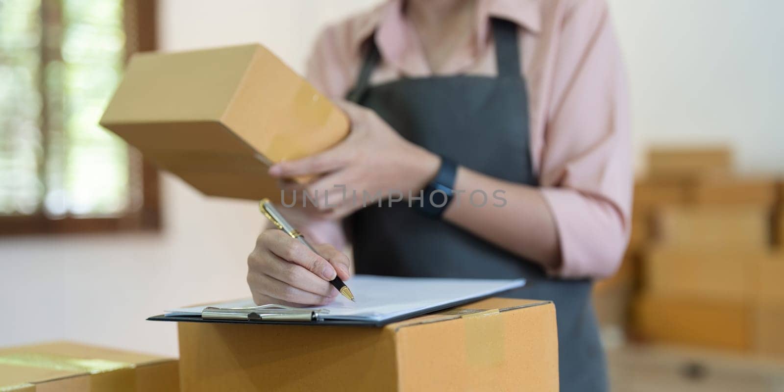 Asian woman entrepreneur prepare parcel box and check online order on laptop computer for commercial checking delivery. online marketing, packing box, SME seller. startup business concept by nateemee
