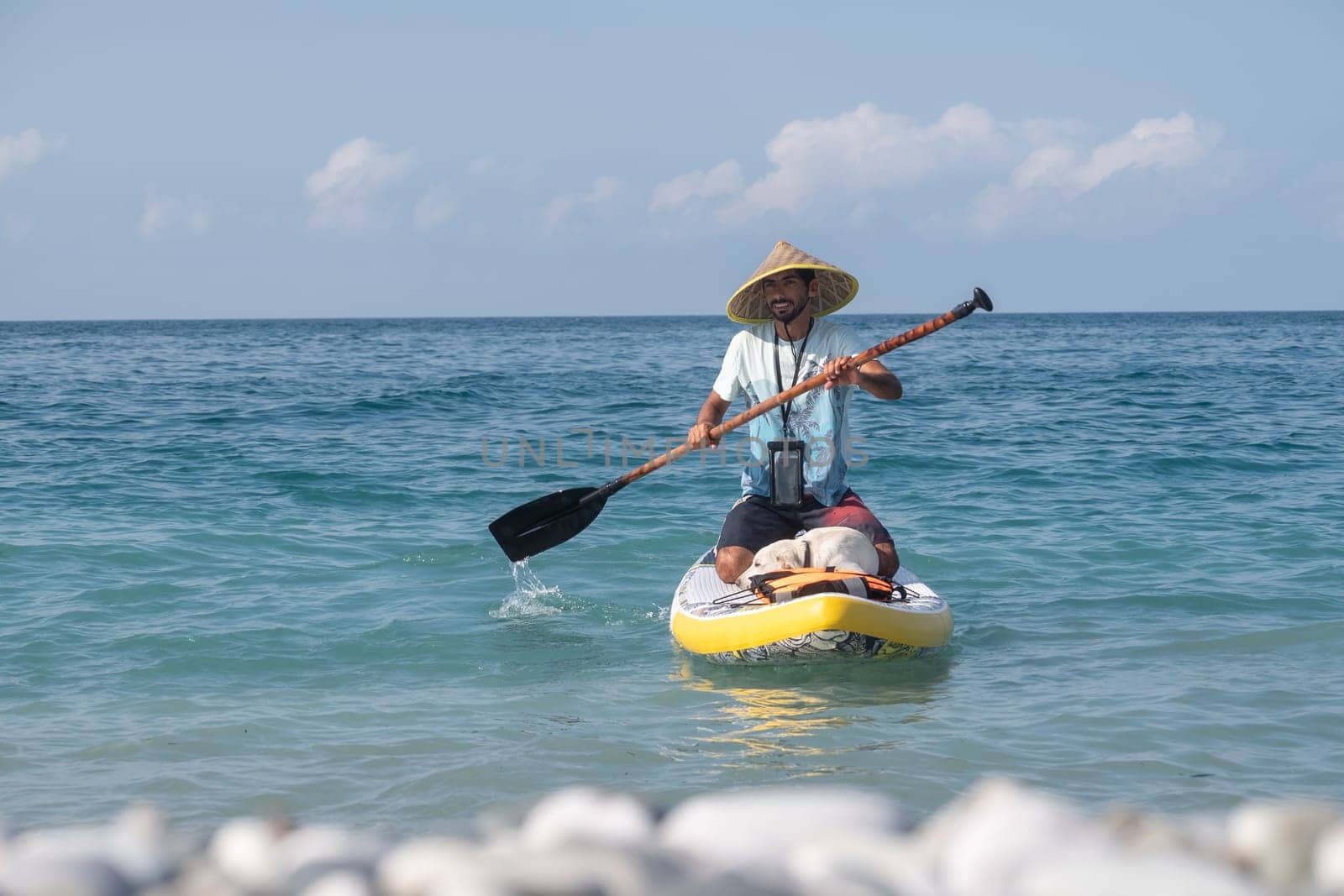 guy on a sup board with a paddle with a dog stands on the sea in summer
