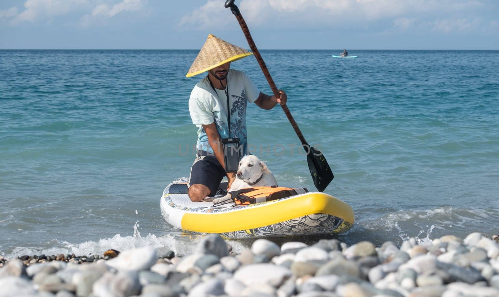 a guy on a sup board with a paddle with a dog stands on the sea in summer by Rotozey