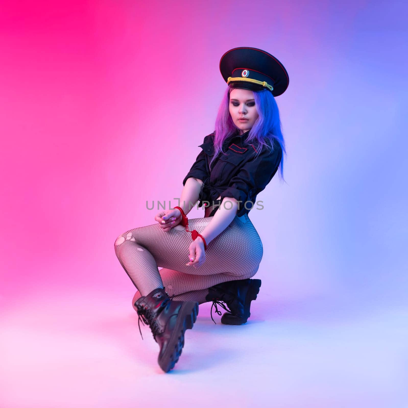An appetizing girl in a sexy police uniform for sexual games with handcuffs in neon light on a light background copy paste