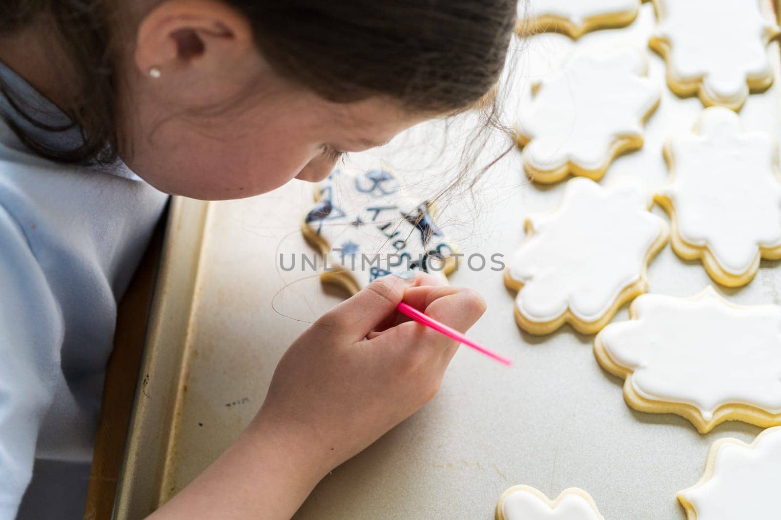 A heartwarming scene of a little girl carefully writing 'Sorry' on sugar cookies with food coloring, the cookies beautifully flooded with white royal icing.