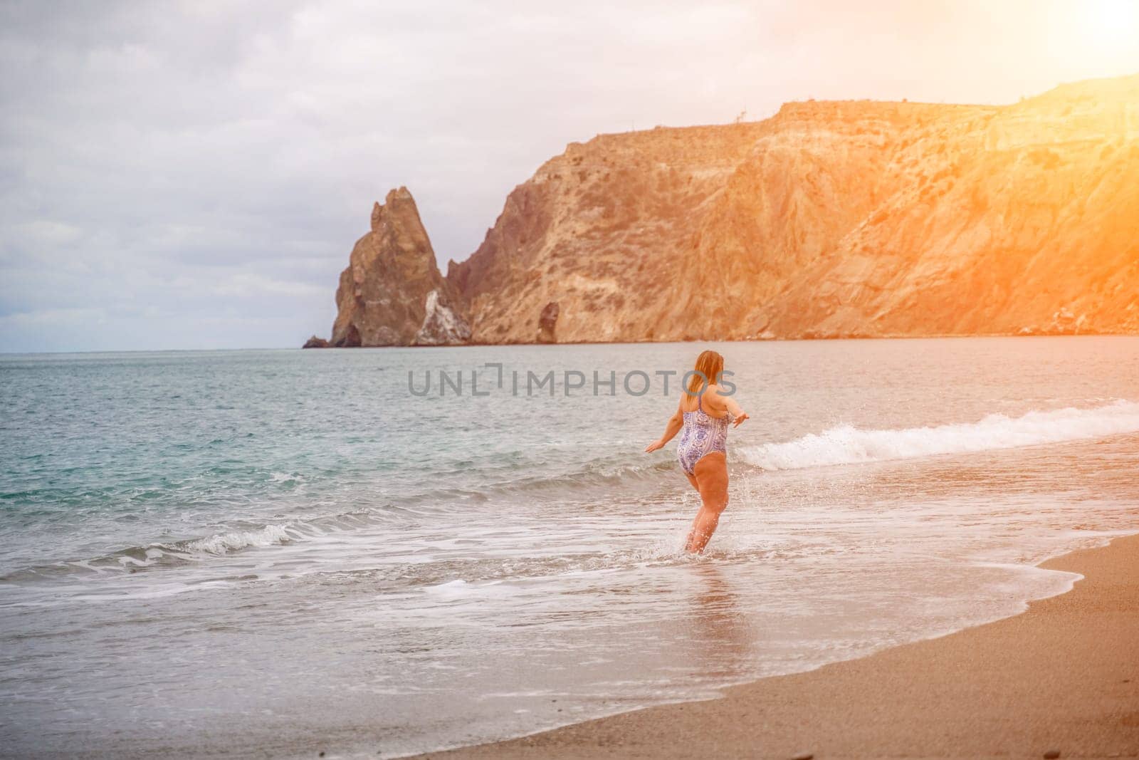 A plump woman in a bathing suit enters the water during the surf. Alone on the beach, Gray sky in the clouds, swimming in winter