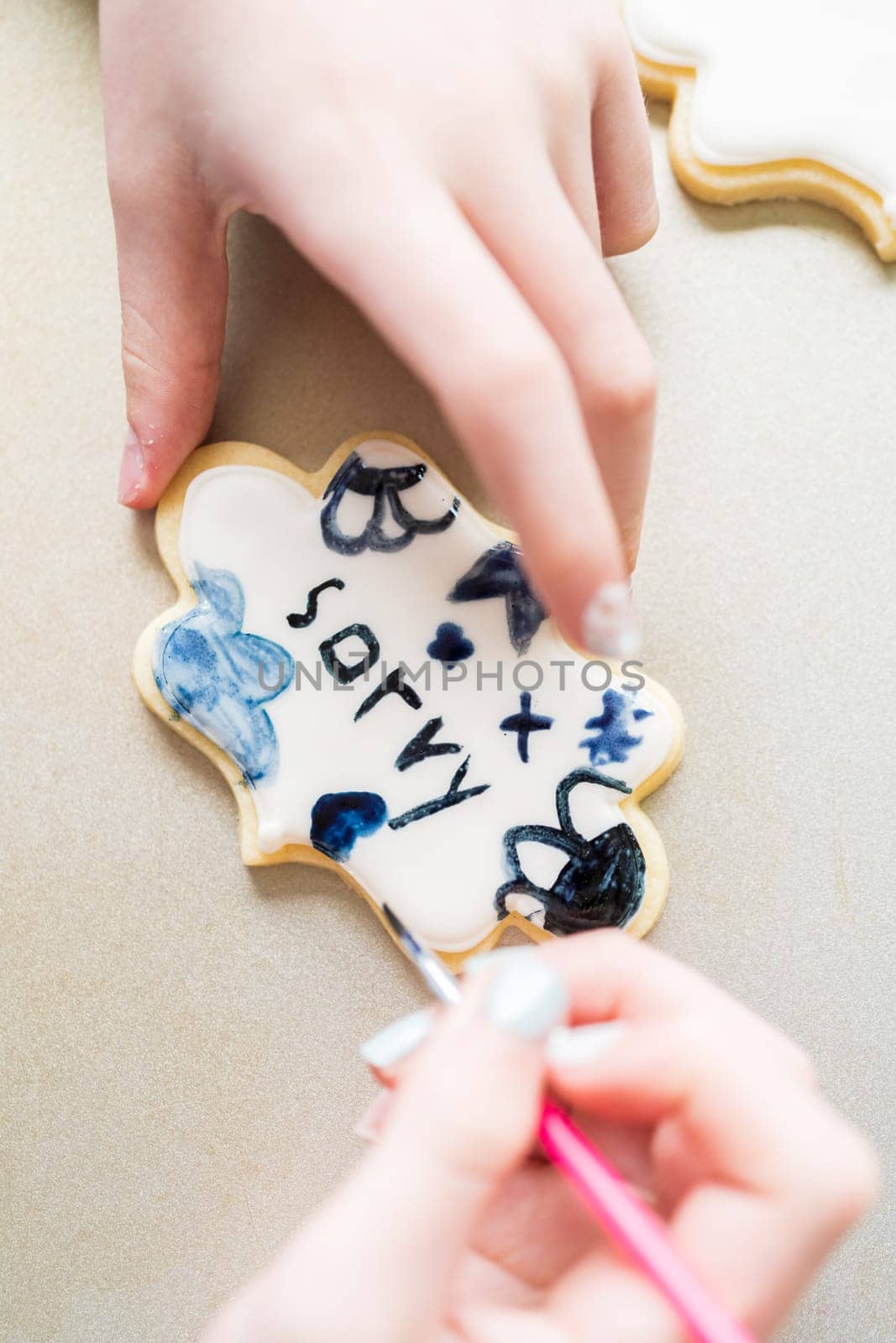 A heartwarming scene of a little girl carefully writing 'Sorry' on sugar cookies with food coloring, the cookies beautifully flooded with white royal icing.